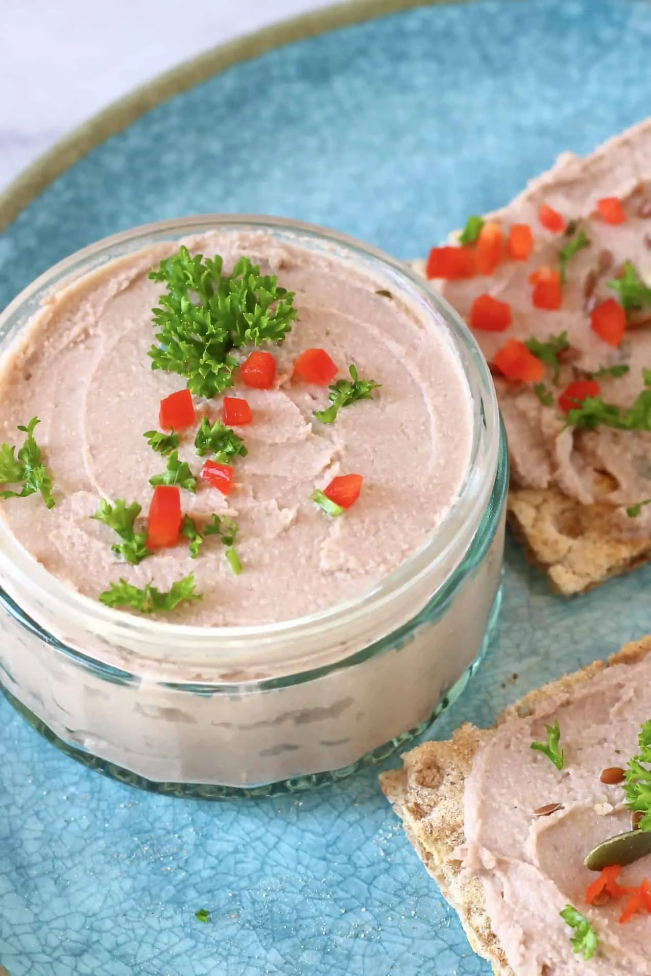 Vegan pâté in a glass jar with two crackers spread with pâté on a blue plate