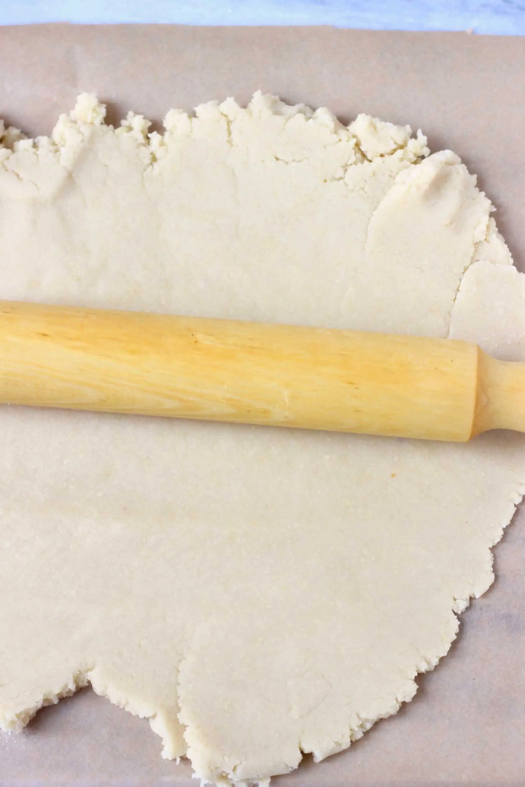 Raw gluten-free vegan sugar cookie dough on baking paper with a rolling pin