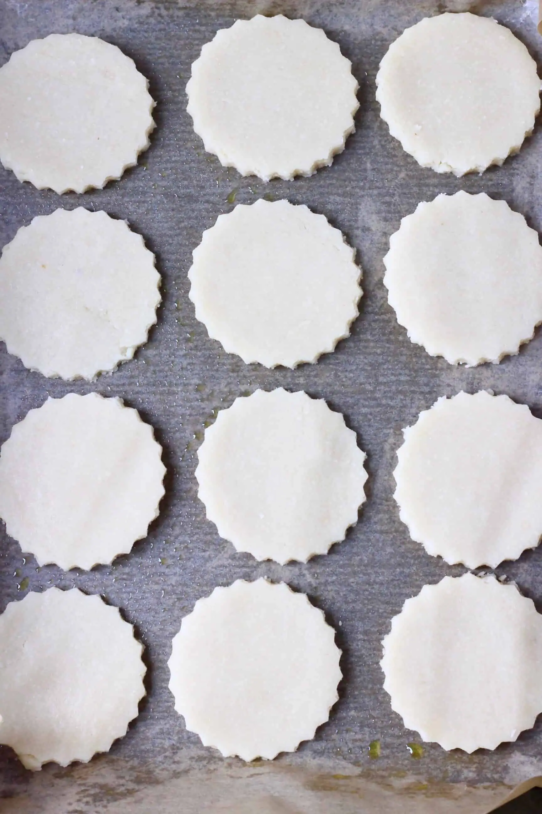 Twelve raw gluten-free vegan sugar cookies on a sheet of brown baking paper