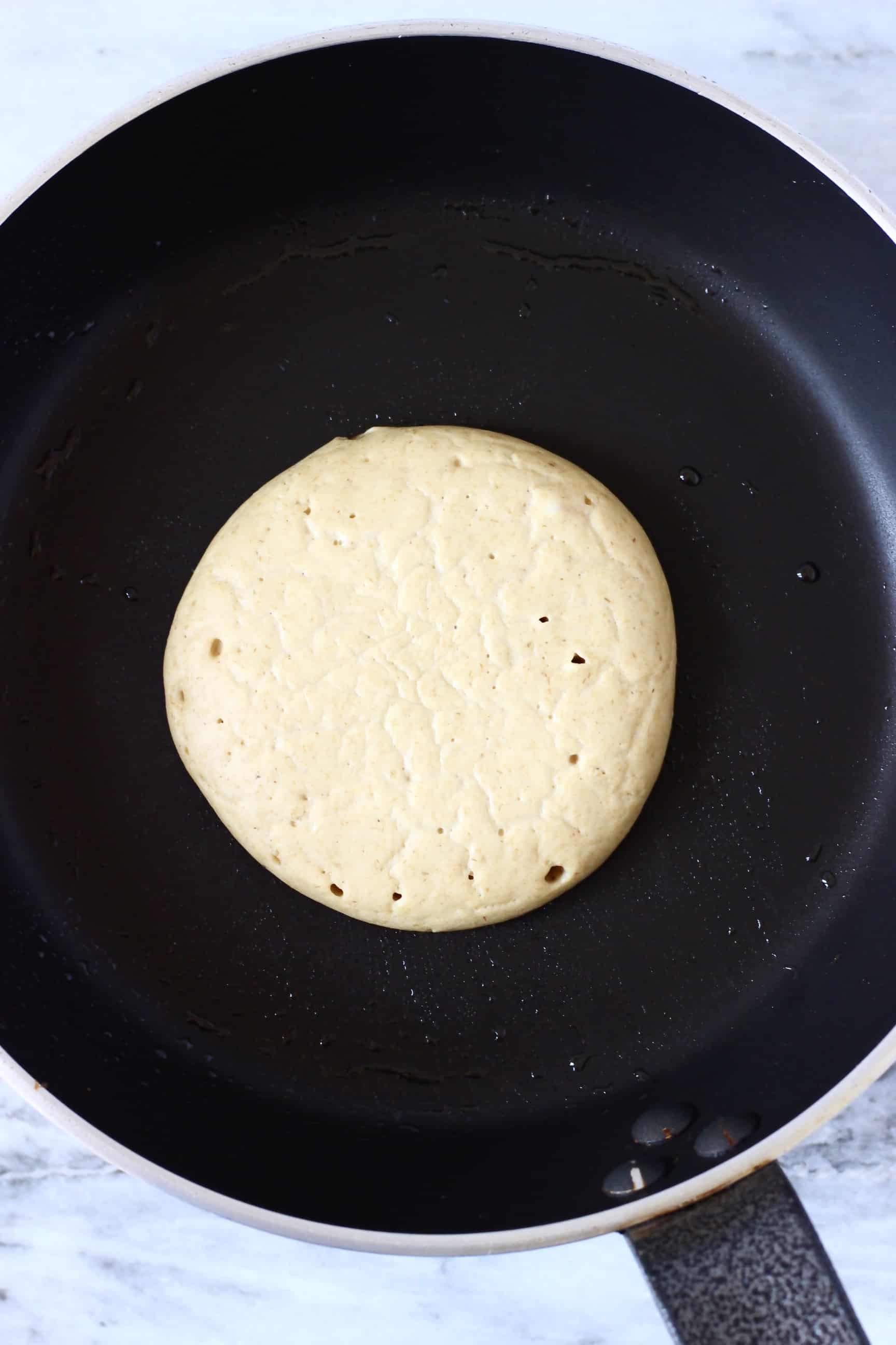 An uncooked gluten-free vegan protein pancake in a frying pan