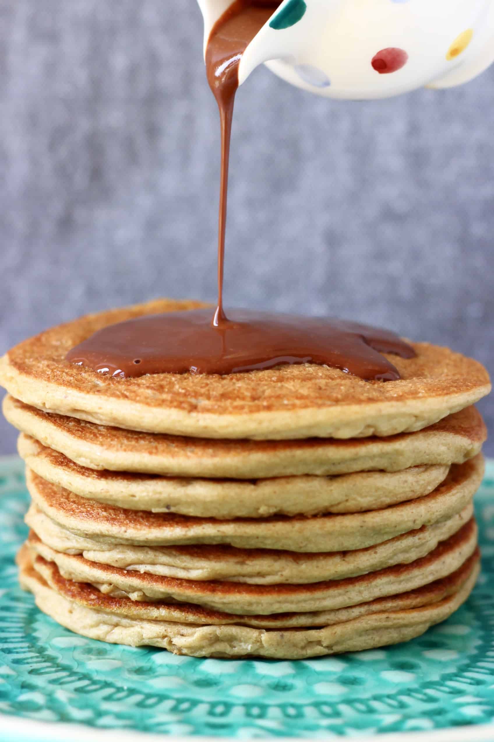 A stack of gluten-free vegan protein pancakes on a blue plate with chocolate sauce being poured on top