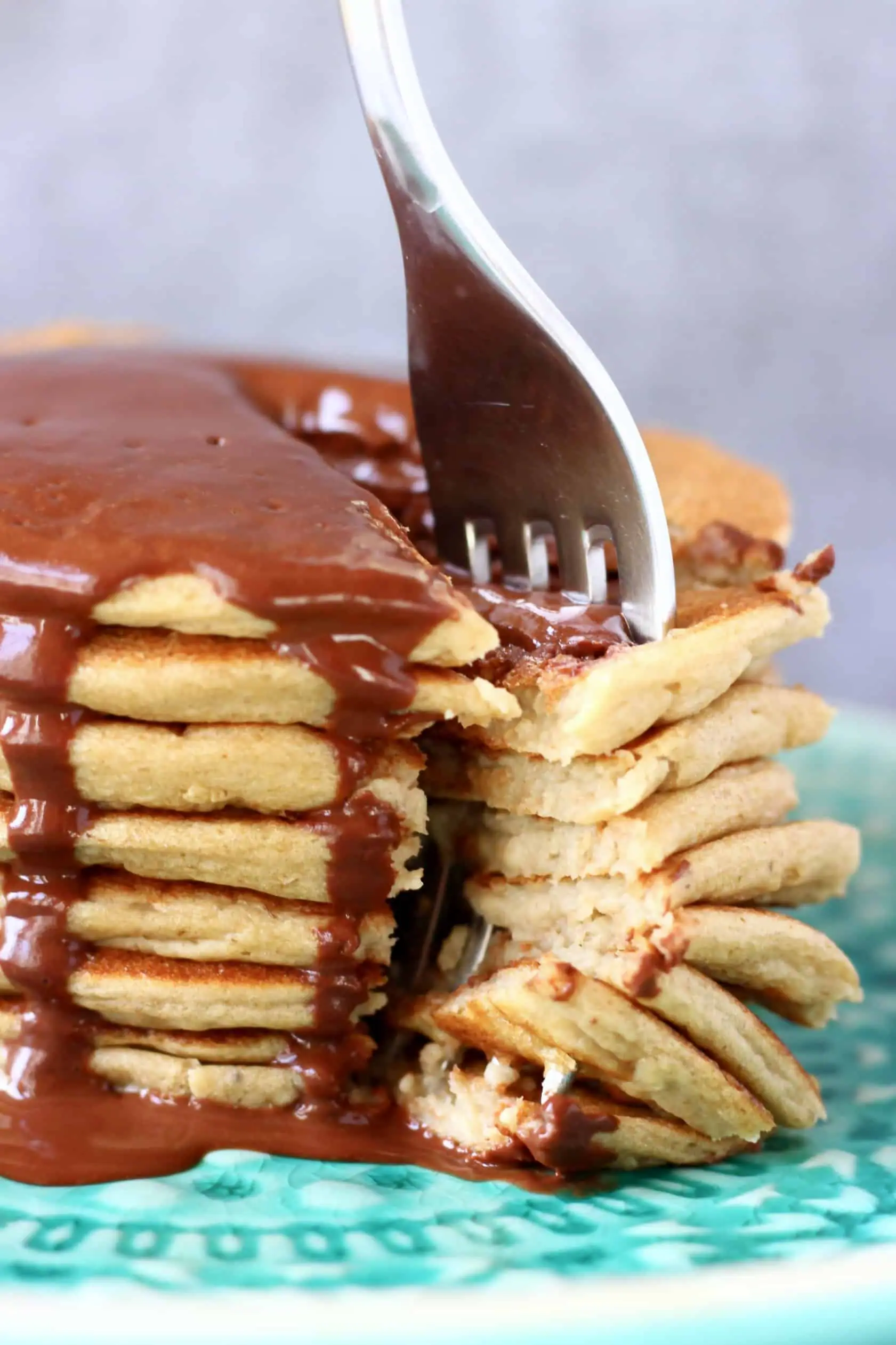 A stack of gluten-free vegan protein pancakes covered in chocolate sauce with fork sticking into them