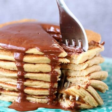 A stack of gluten-free vegan protein pancakes covered in chocolate sauce with a fork sticking into it