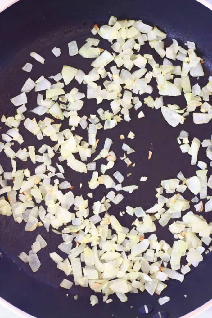 Photo of diced onion pieces cooking in a black frying pan