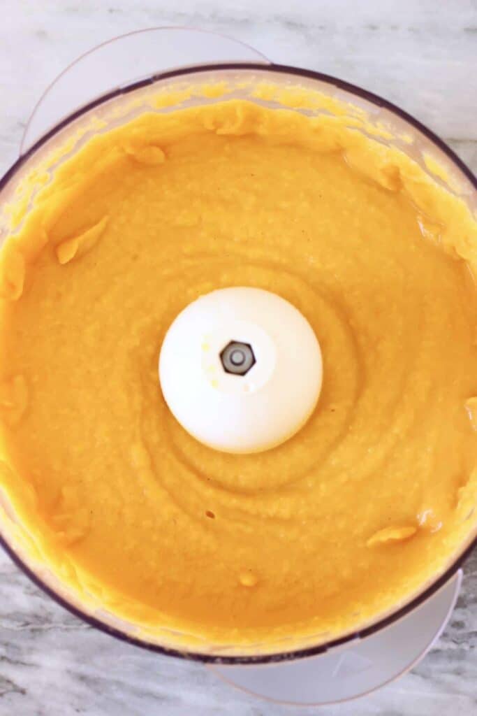 Photo of orange butternut squash sauce in a food processor against a marble background