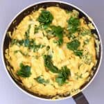 Photo of pasta with orange butternut squash sauce and green kale in a black frying pan against a grey background