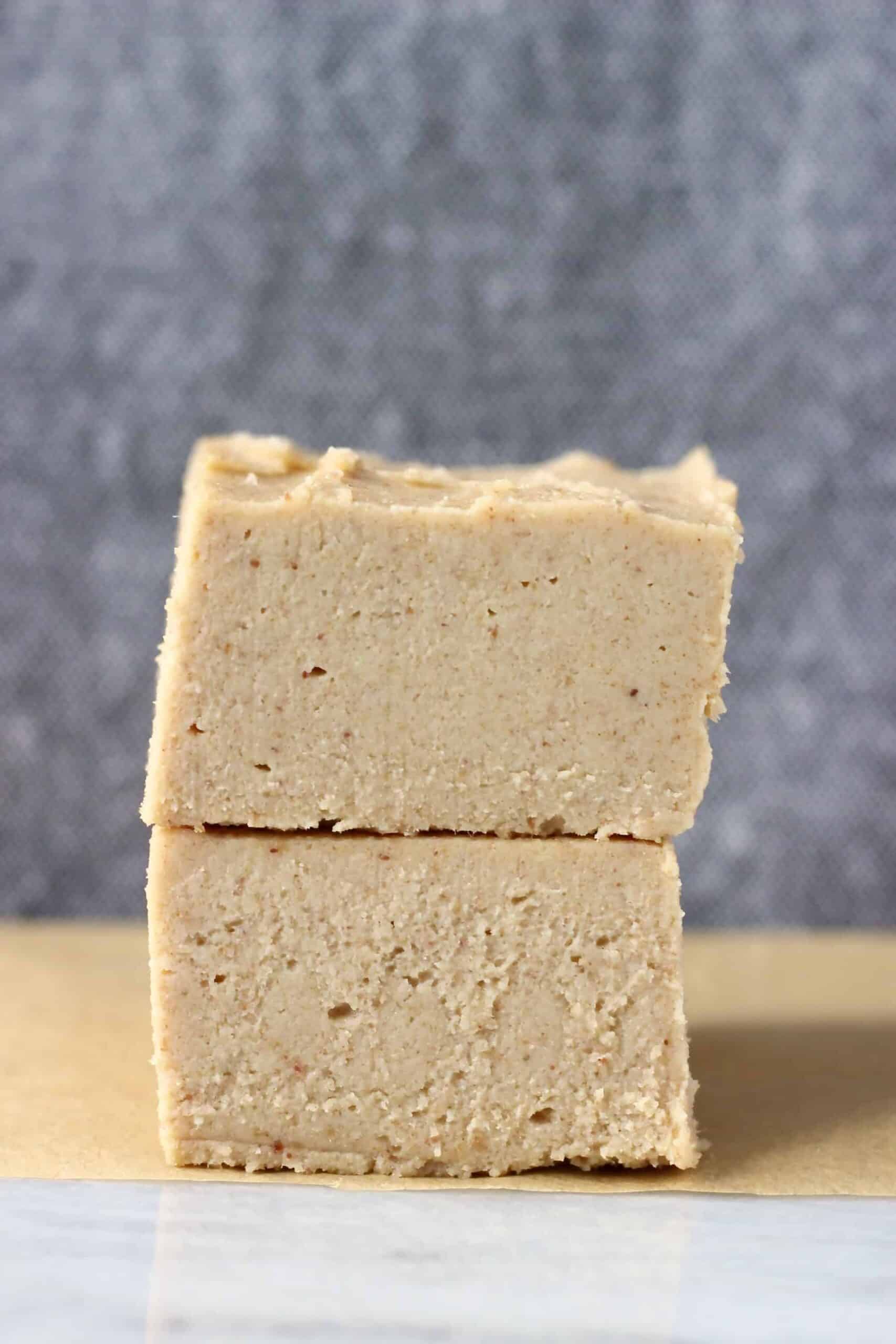 Two squares of caramel-coloured vegan fudge on a marble slab