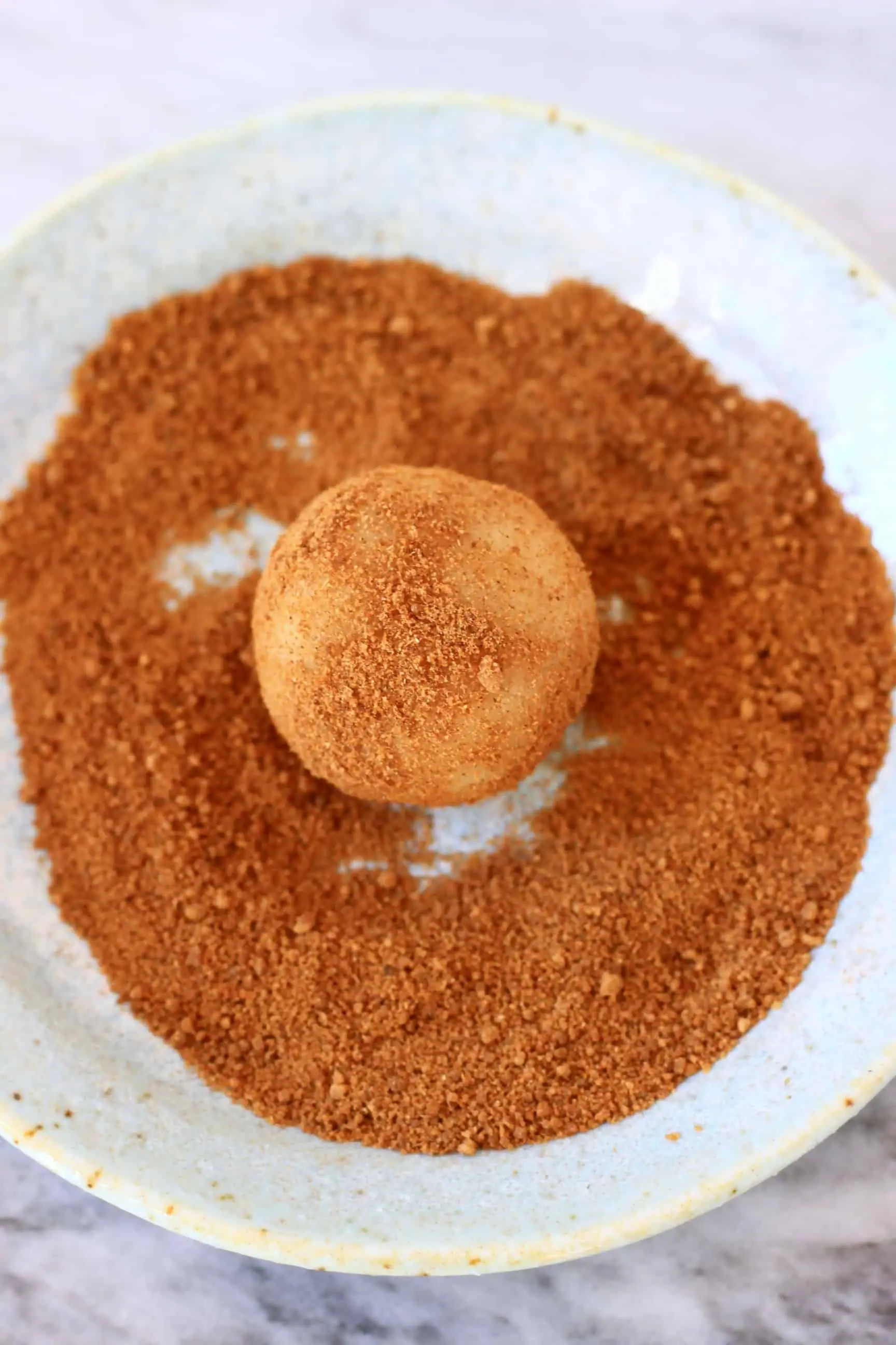 Cinnamon sugar on a plate with a ball of gluten-free vegan snickerdoodles cookie dough being rolled in the sugar