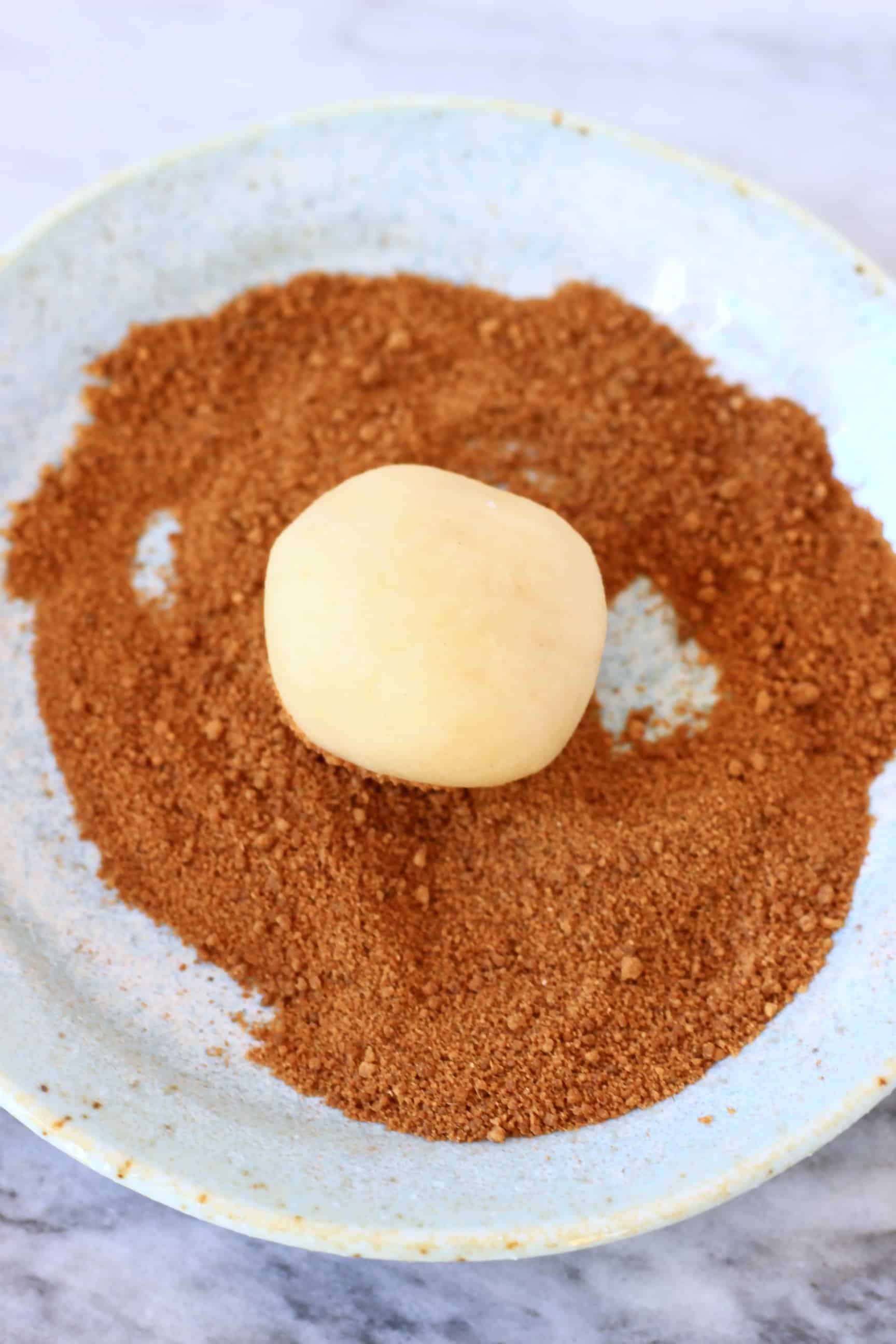 Cinnamon sugar on a plate with a ball of white gluten-free vegan snickerdoodles cookie dough 
