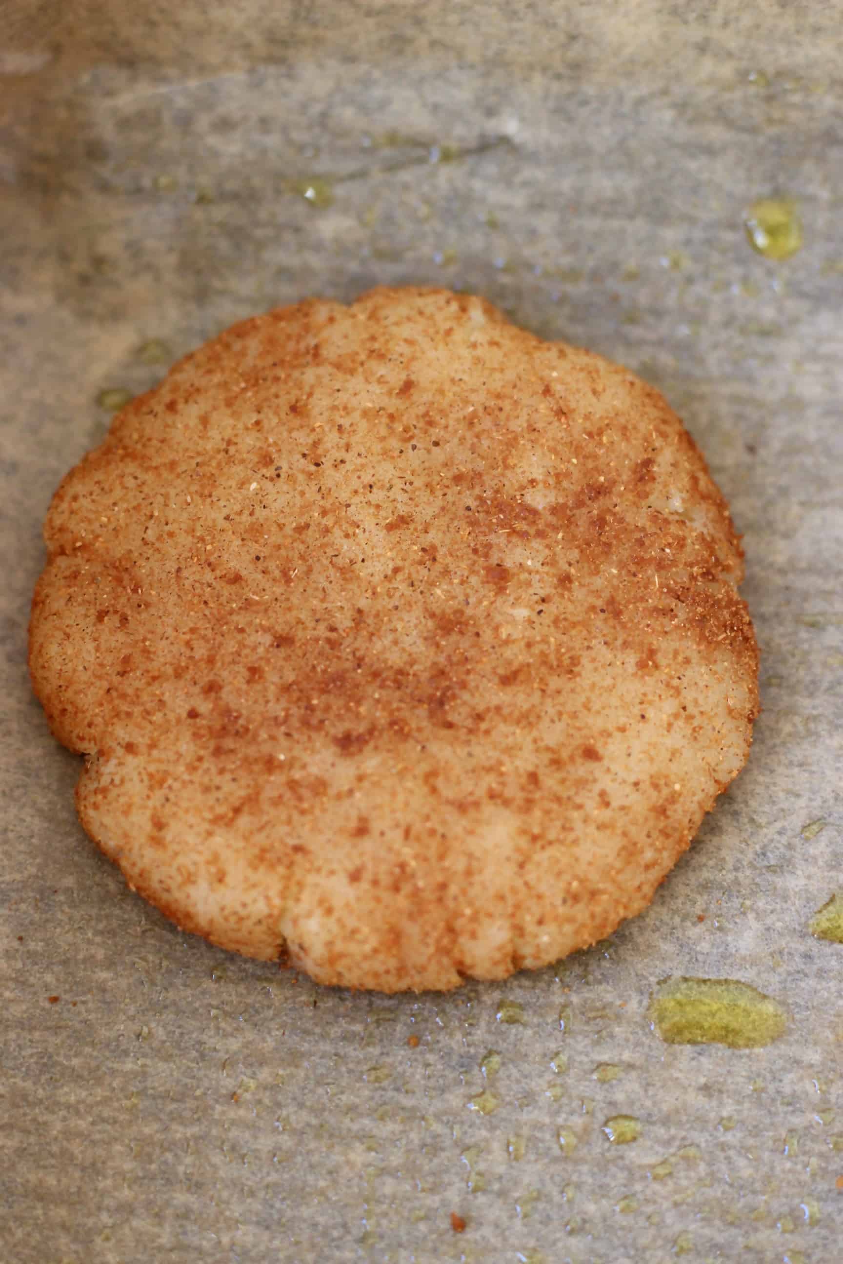 A raw gluten-free vegan snickerdoodle coated in cinnamon sugar on a sheet of baking paper