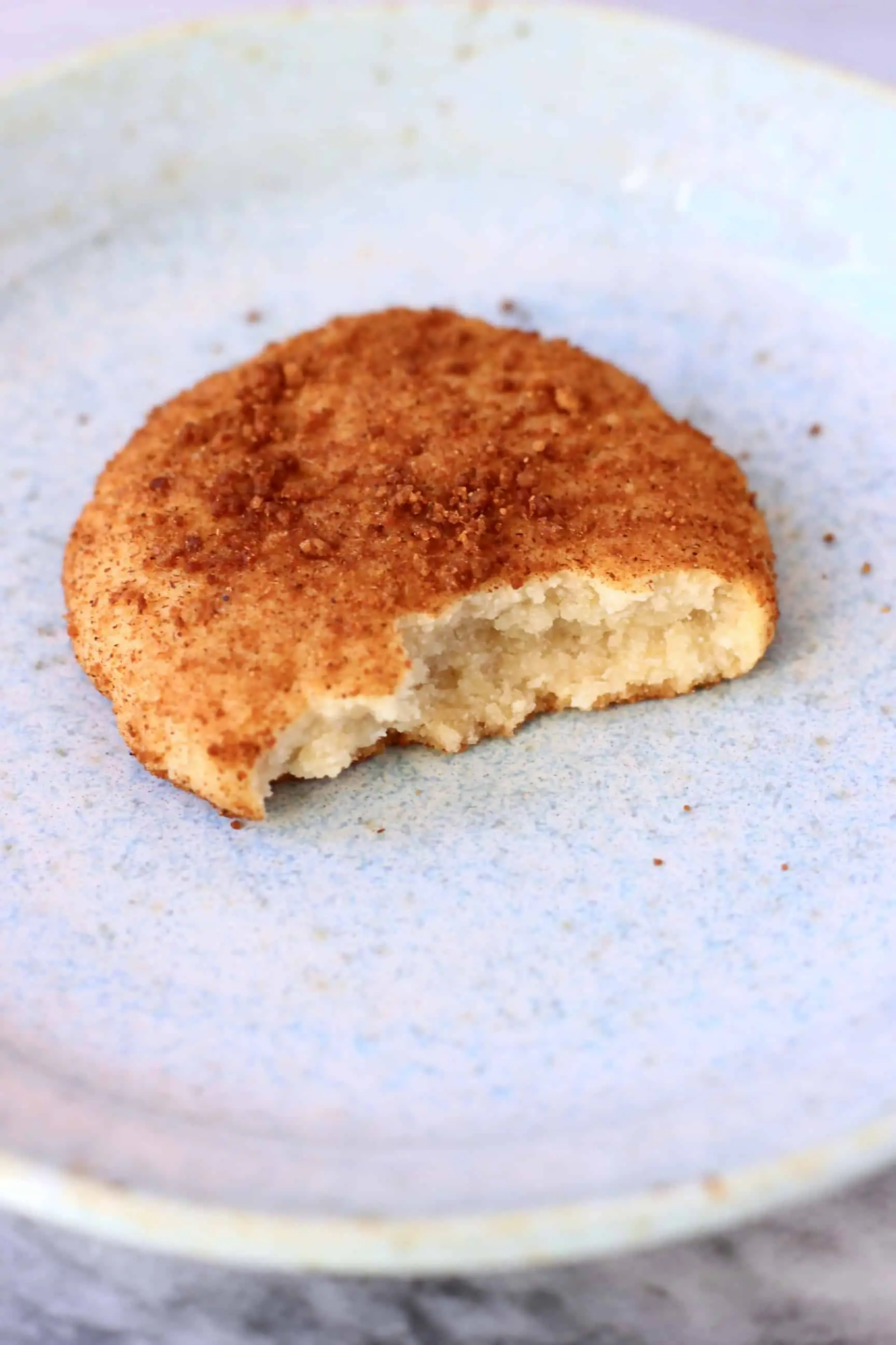 A gluten-free vegan snickerdoodle cookie with a bite taken out of it on a plate 