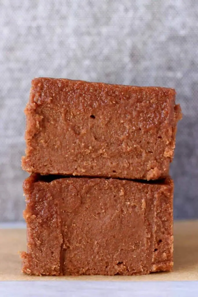Photo of two squares of chocolate fudge on a sheet of brown baking paper against a grey background