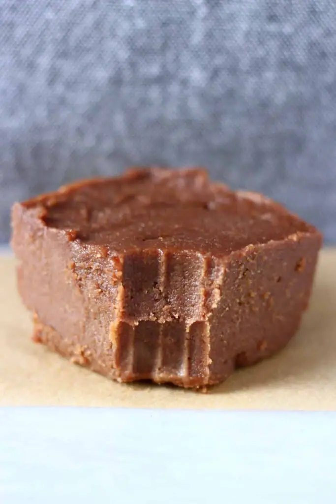 Photo of a square of chocolate fudge with a bite taken out of it on a piece of brown baking paper against a grey background