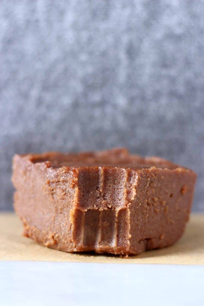 Photo of a square of chocolate fudge with a bite taken out of it on a piece of brown baking paper against a grey background