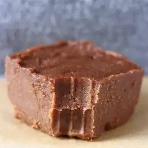 Photo of a square of chocolate fudge with a bite taken out of it on a piece of brown baking paper against a grey background