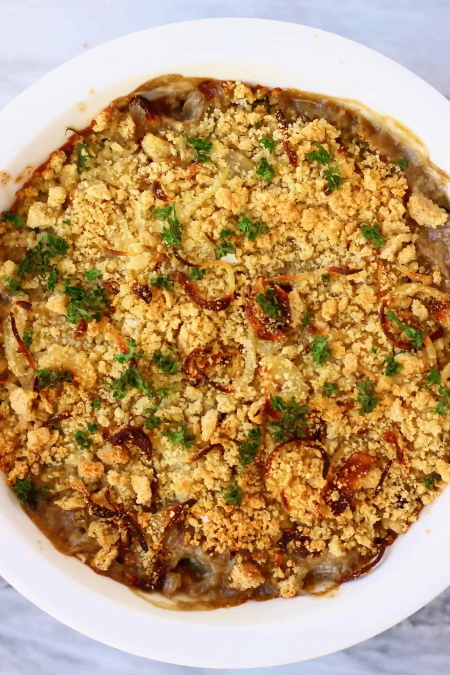 Vegan green bean casserole topped with golden brown breadcrumbs and green parsley in pie dish