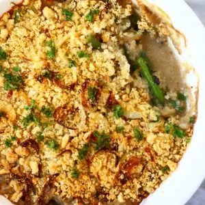 Vegan green bean casserole topped with golden brown breadcrumbs in a pie dish with a mouthful taken out of it