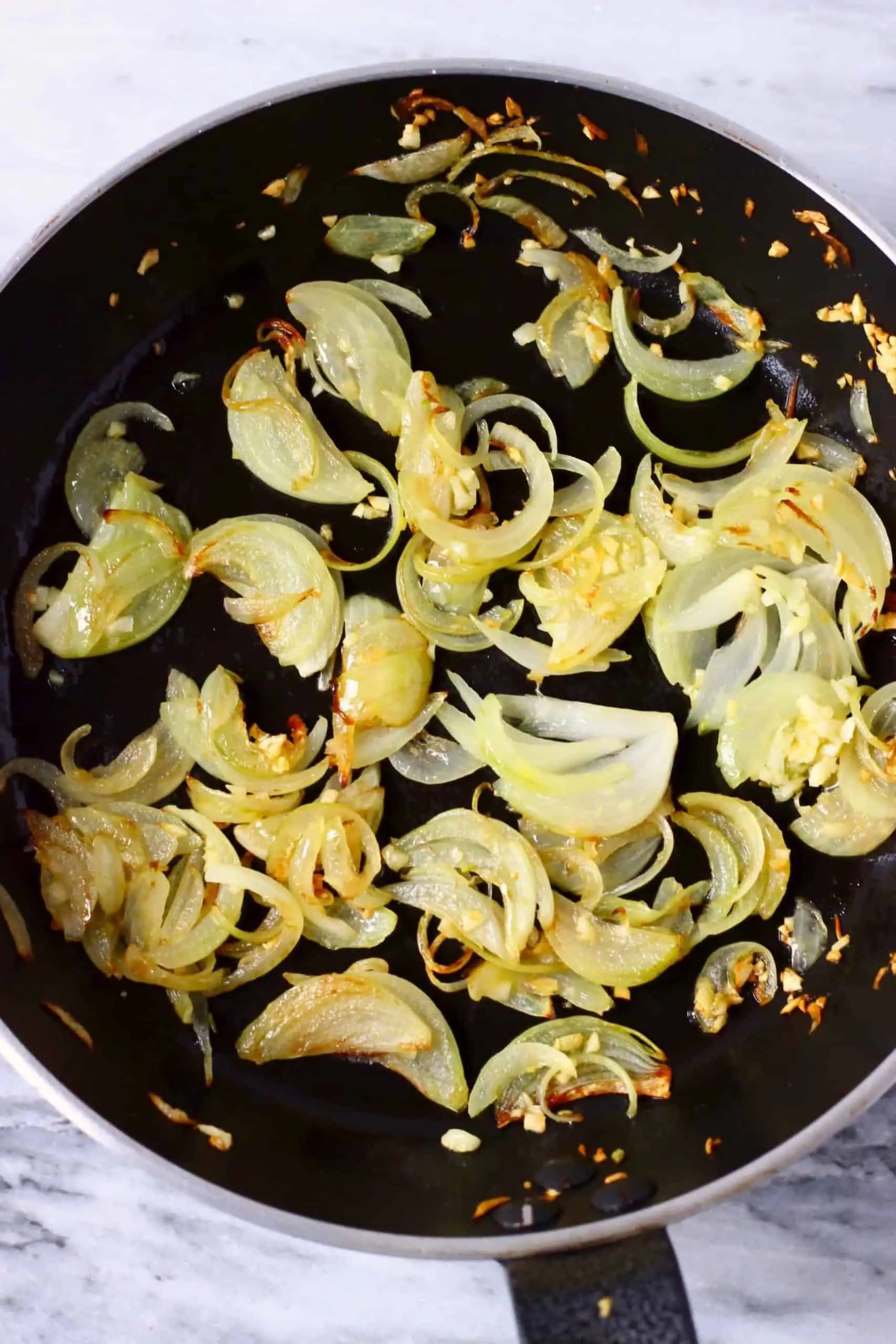 Sliced onions and minced garlic being fried in a frying pan