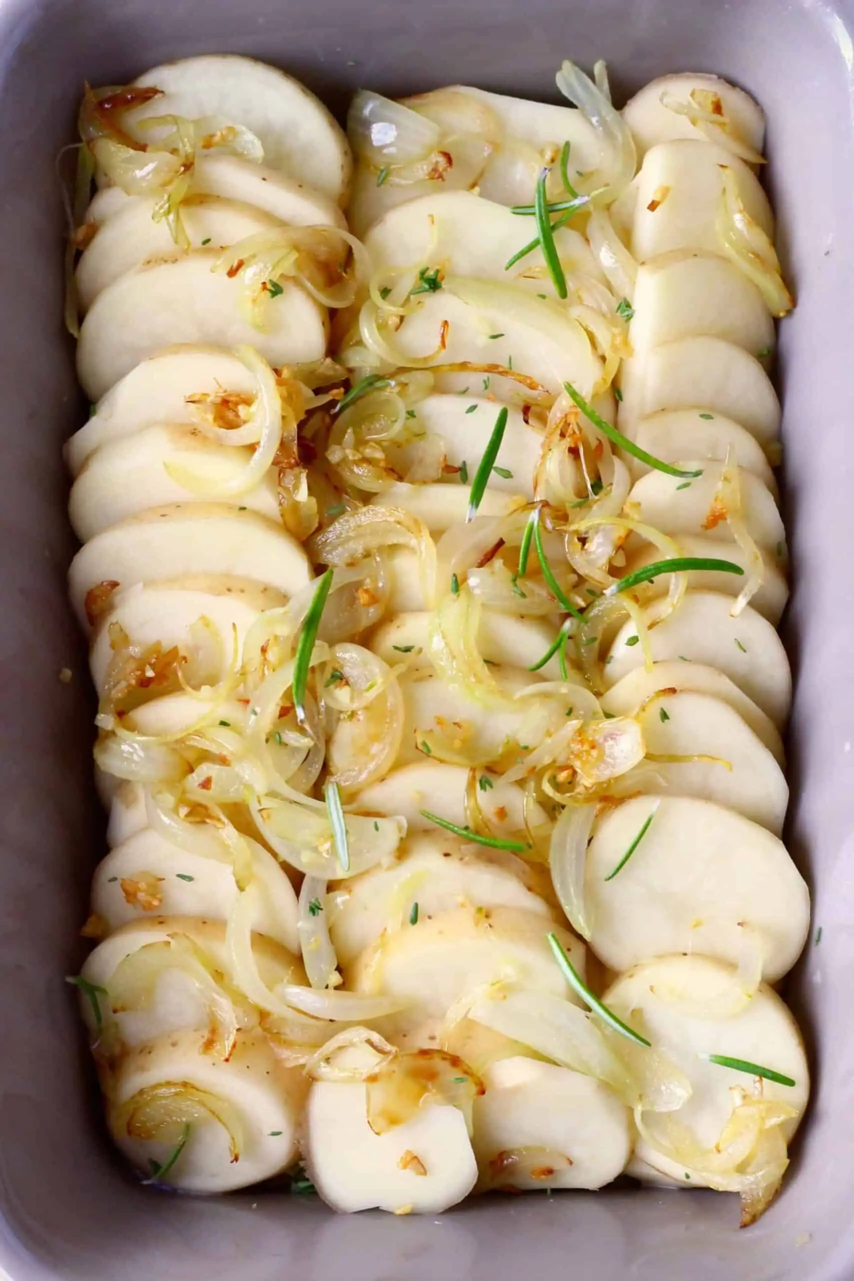 Sliced potatoes topped with fried onions and green herbs in a baking dish