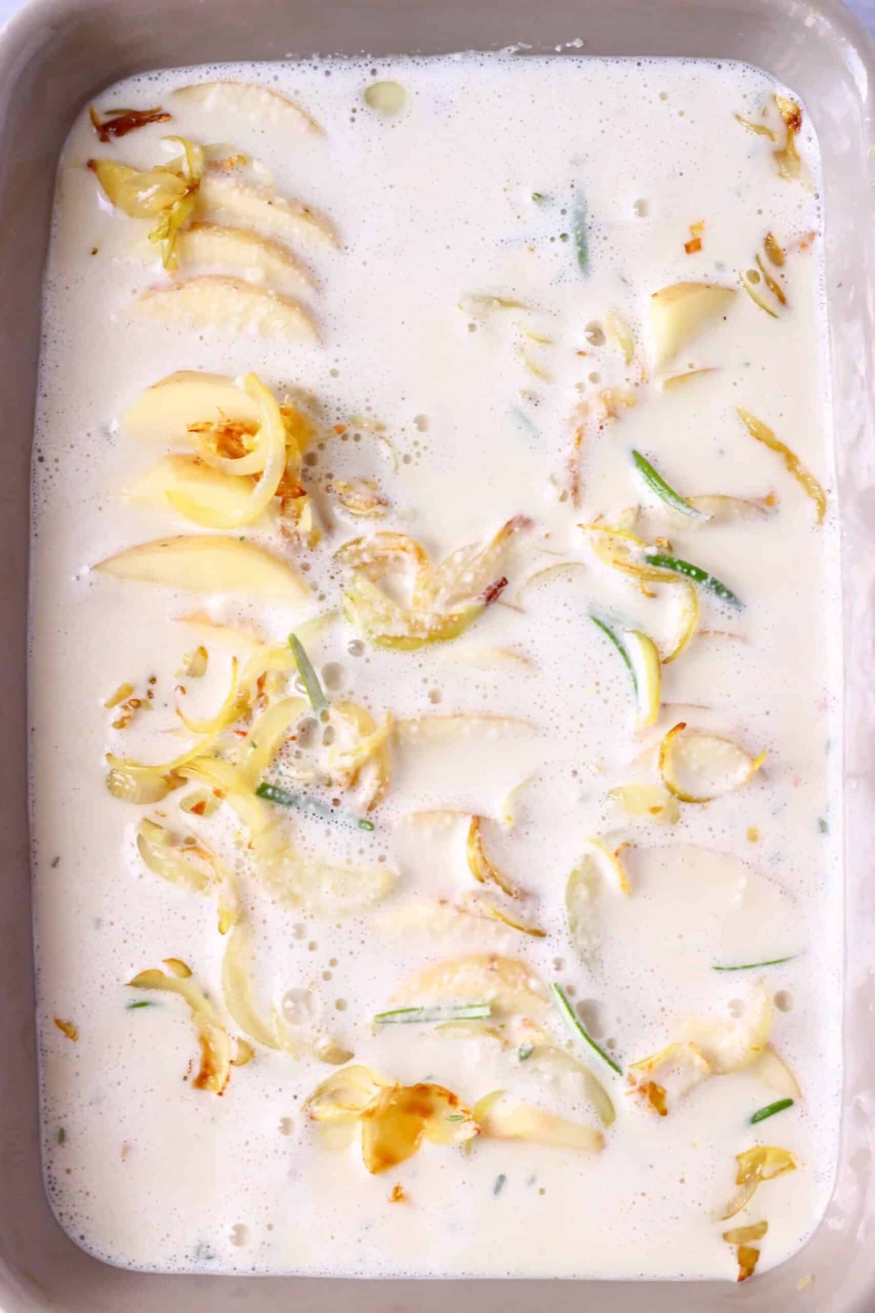 Sliced potatoes with fried onions and green herbs covered in white cream in a baking dish