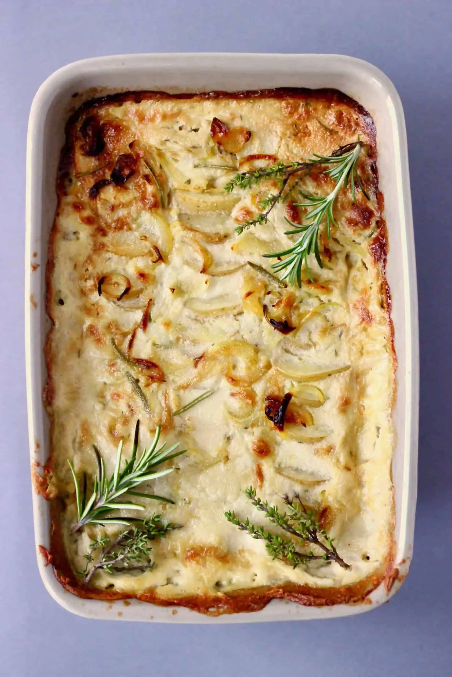Vegan scalloped potatoes topped with thyme and rosemary in a baking dish