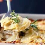 Vegan scalloped potatoes in a baking dish with a spoon lifting up a mouthful of it