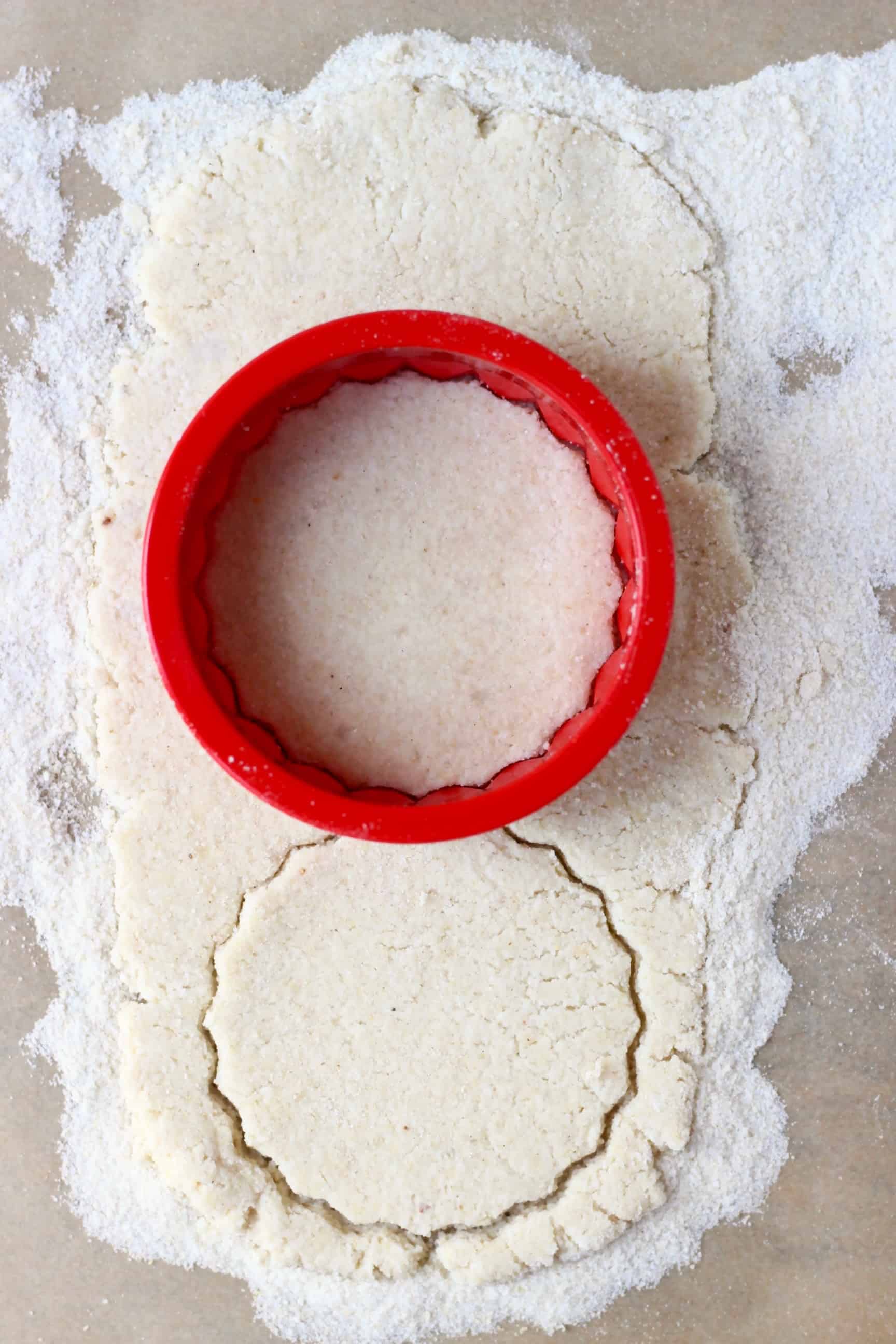 These Gluten-Free Vegan Mince Pies are crispy, flaky, fruity and fragrant - the best festive sweet treat for Christmas! Dairy-free, vegetarian, egg-free and refined sugar free. #rhiansrecipes #christmas #mincepies #vegan #dairyfree #glutenfree #dessert Gluten-free vegan pastry dough rolled out on a sheet of baking paper with a circular cookie cutter on it