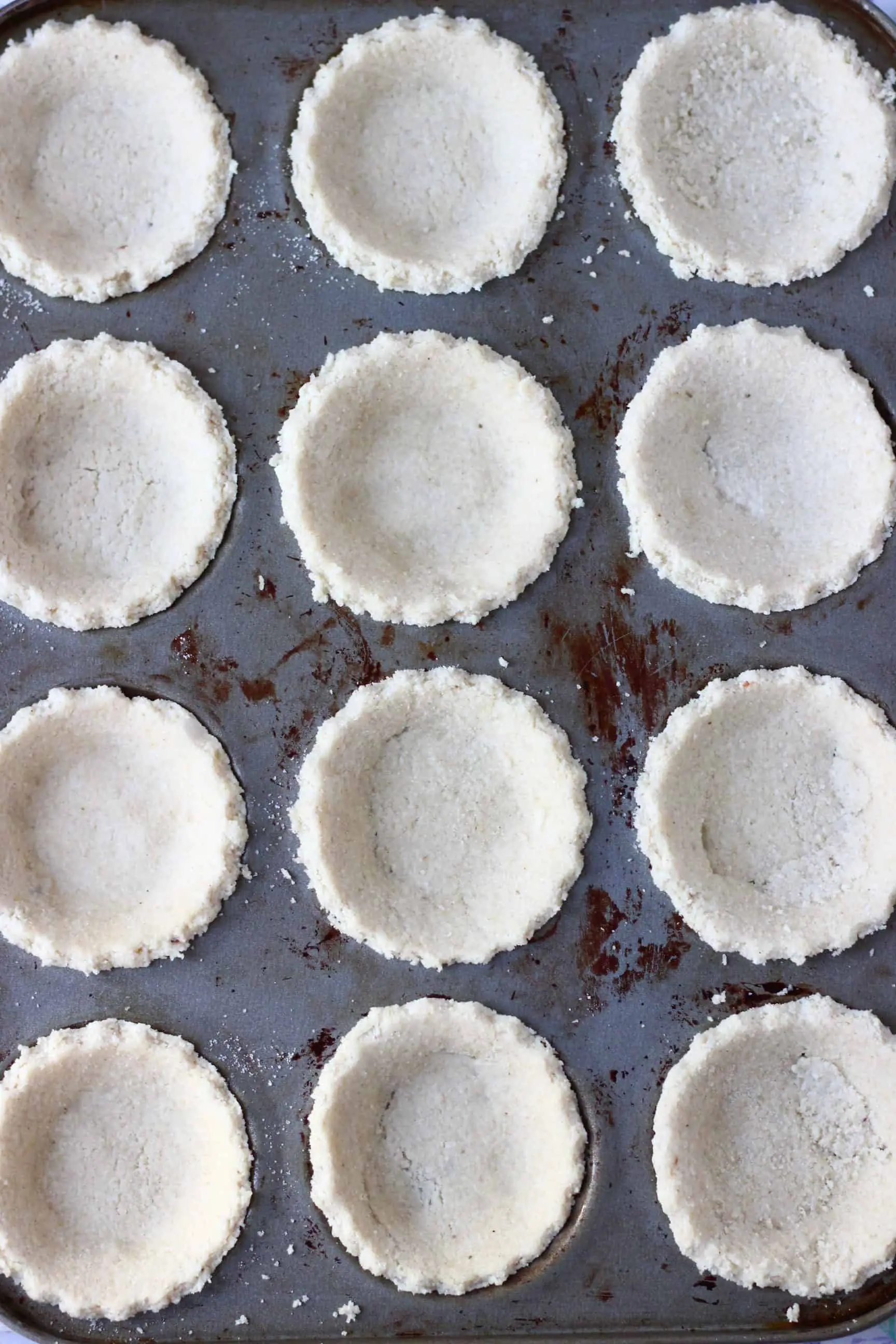 Twelve gluten-free vegan mince pies pastry crusts in a muffin tin 