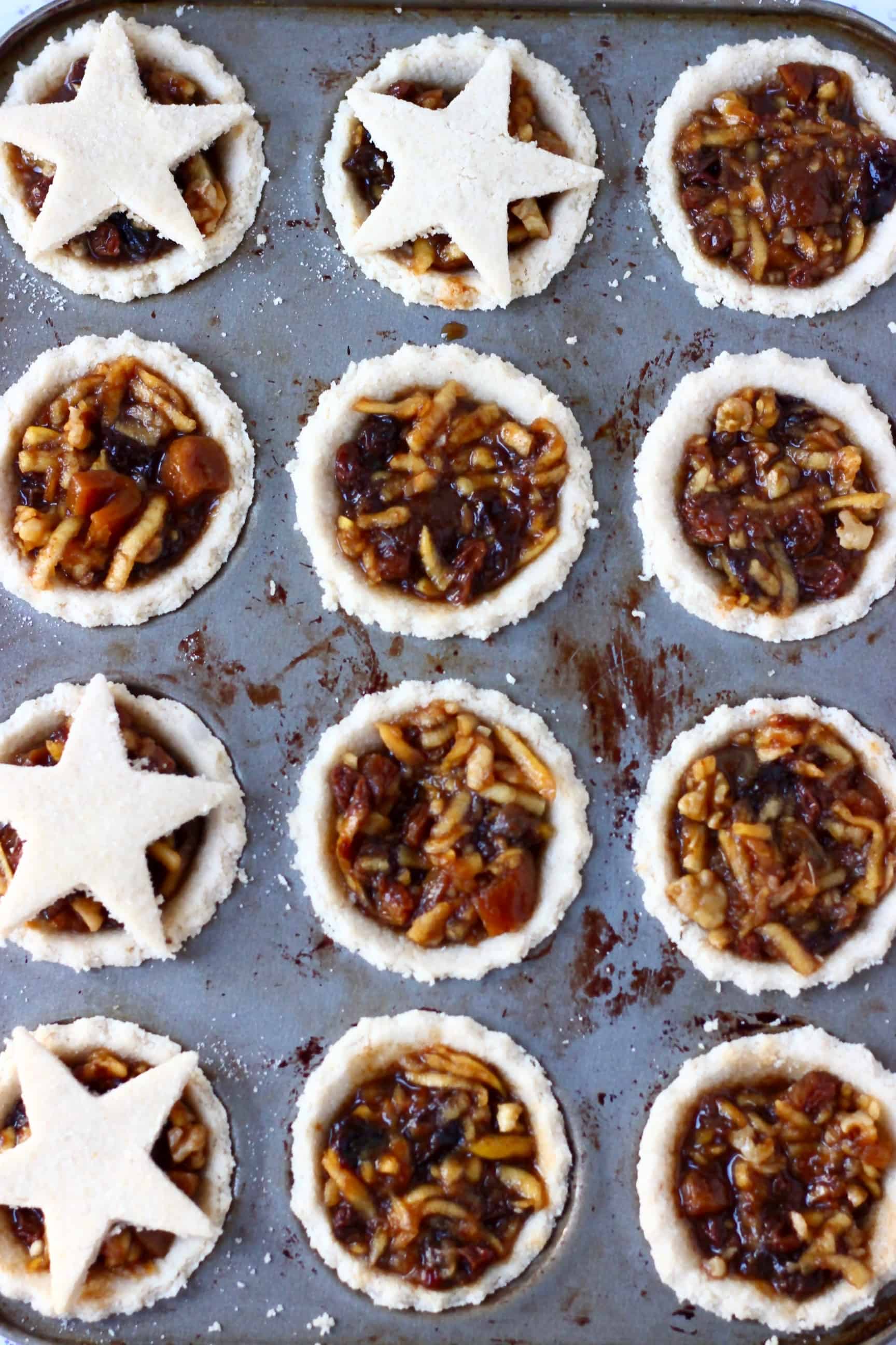 These Gluten-Free Vegan Mince Pies are crispy, flaky, fruity and fragrant - the best festive sweet treat for Christmas! Dairy-free, vegetarian, egg-free and refined sugar free. #rhiansrecipes #christmas #mincepies #vegan #dairyfree #glutenfree #dessert Twelve gluten-free vegan mince pies pastry crusts in a muffin tin filled with vegan mincemeat