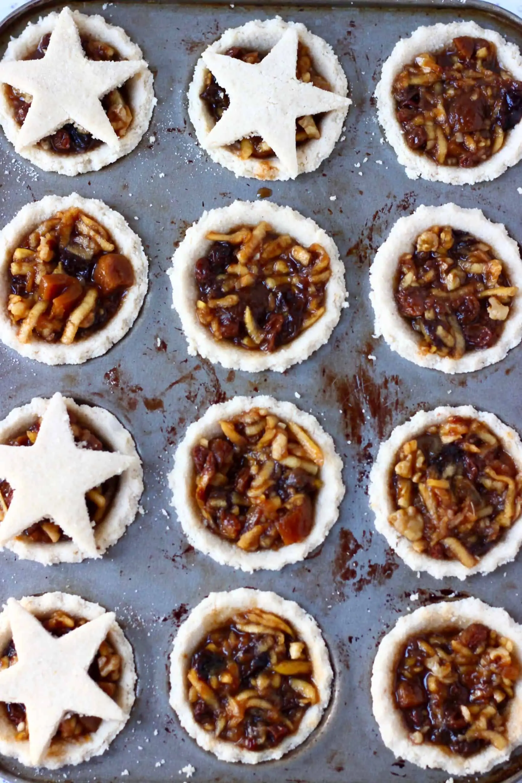 Twelve gluten-free vegan mince pies pastry crusts in a muffin tin filled with vegan mincemeat 