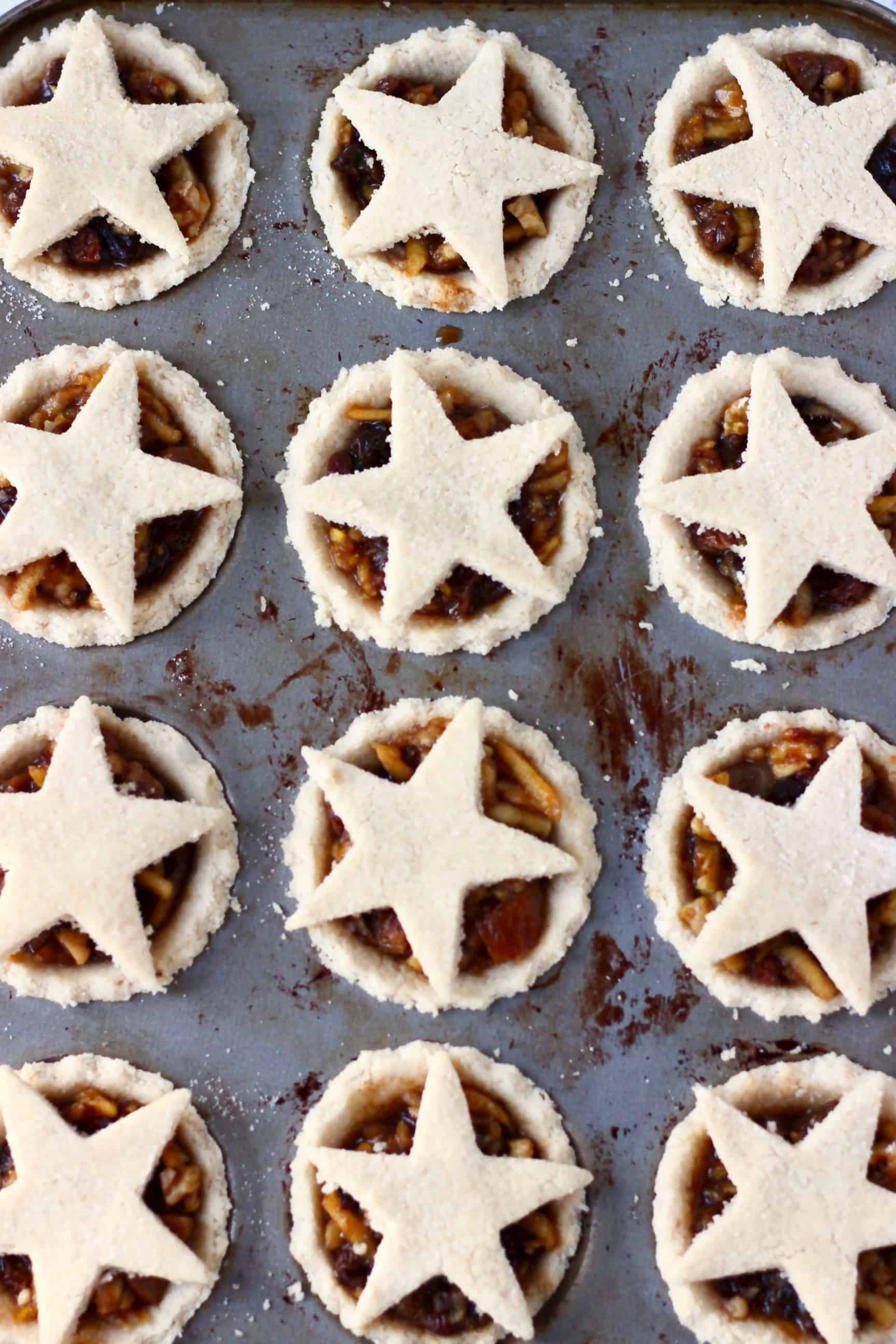 These Gluten-Free Vegan Mince Pies are crispy, flaky, fruity and fragrant - the best festive sweet treat for Christmas! Dairy-free, vegetarian, egg-free and refined sugar free. #rhiansrecipes #christmas #mincepies #vegan #dairyfree #glutenfree #dessert Twelve raw gluten-free vegan mince pies pastry crusts in a muffin tin filled with vegan mincemeat and topped with pastry stars