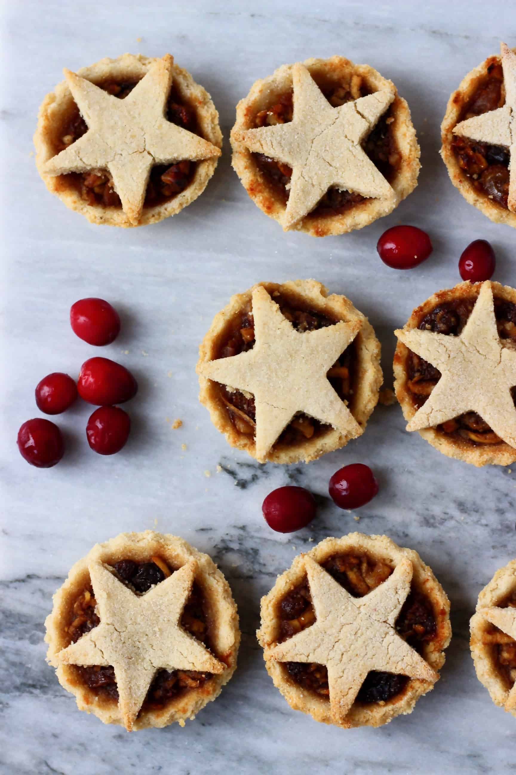 These Gluten-Free Vegan Mince Pies are crispy, flaky, fruity and fragrant - the best festive sweet treat for Christmas! Dairy-free, vegetarian, egg-free and refined sugar free. #rhiansrecipes #christmas #mincepies #vegan #dairyfree #glutenfree #dessert Six gluten-free vegan mince pies topped with pastry stars against a marble background