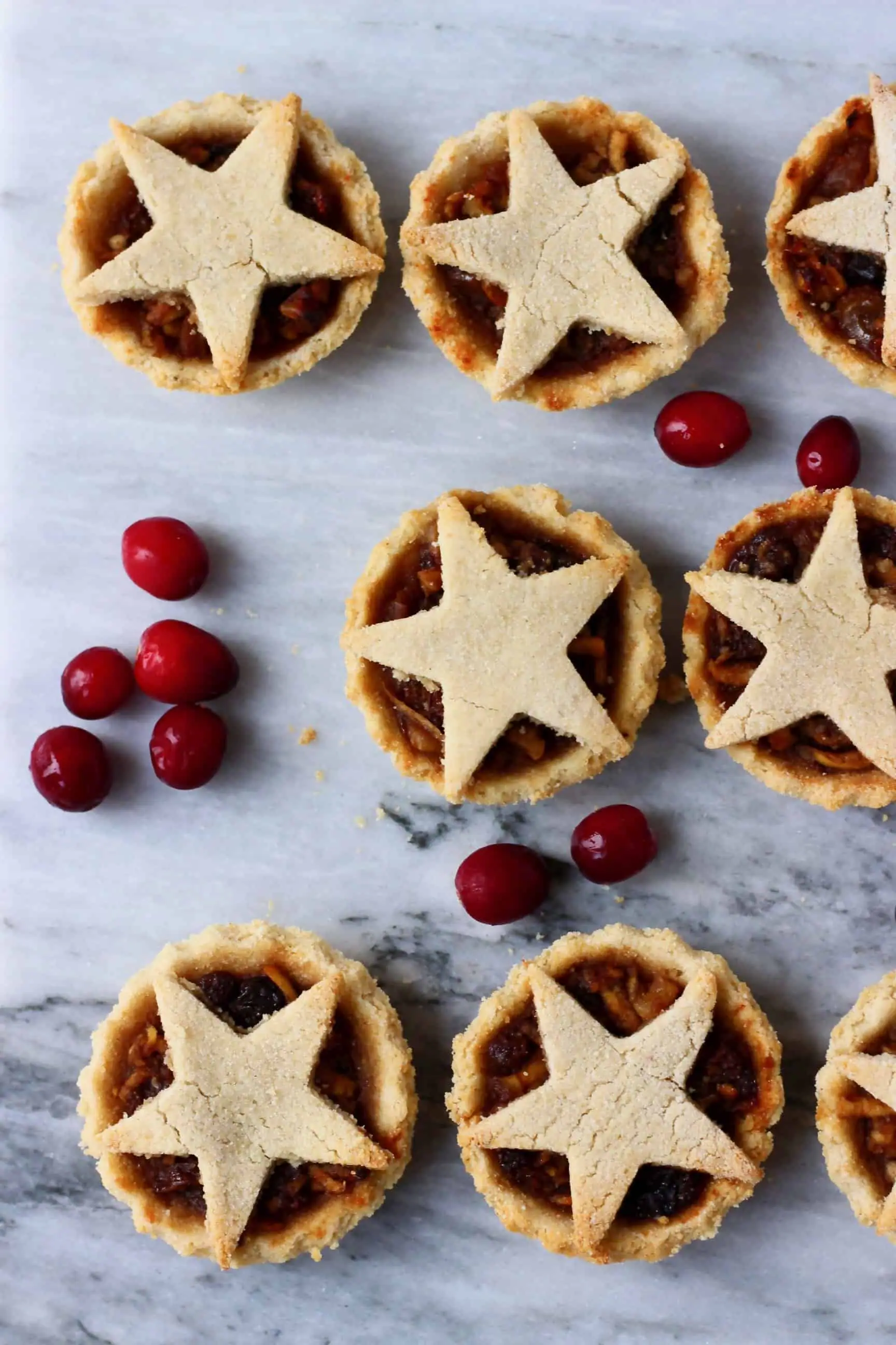 Six gluten-free vegan mince pies topped with pastry stars against a marble background