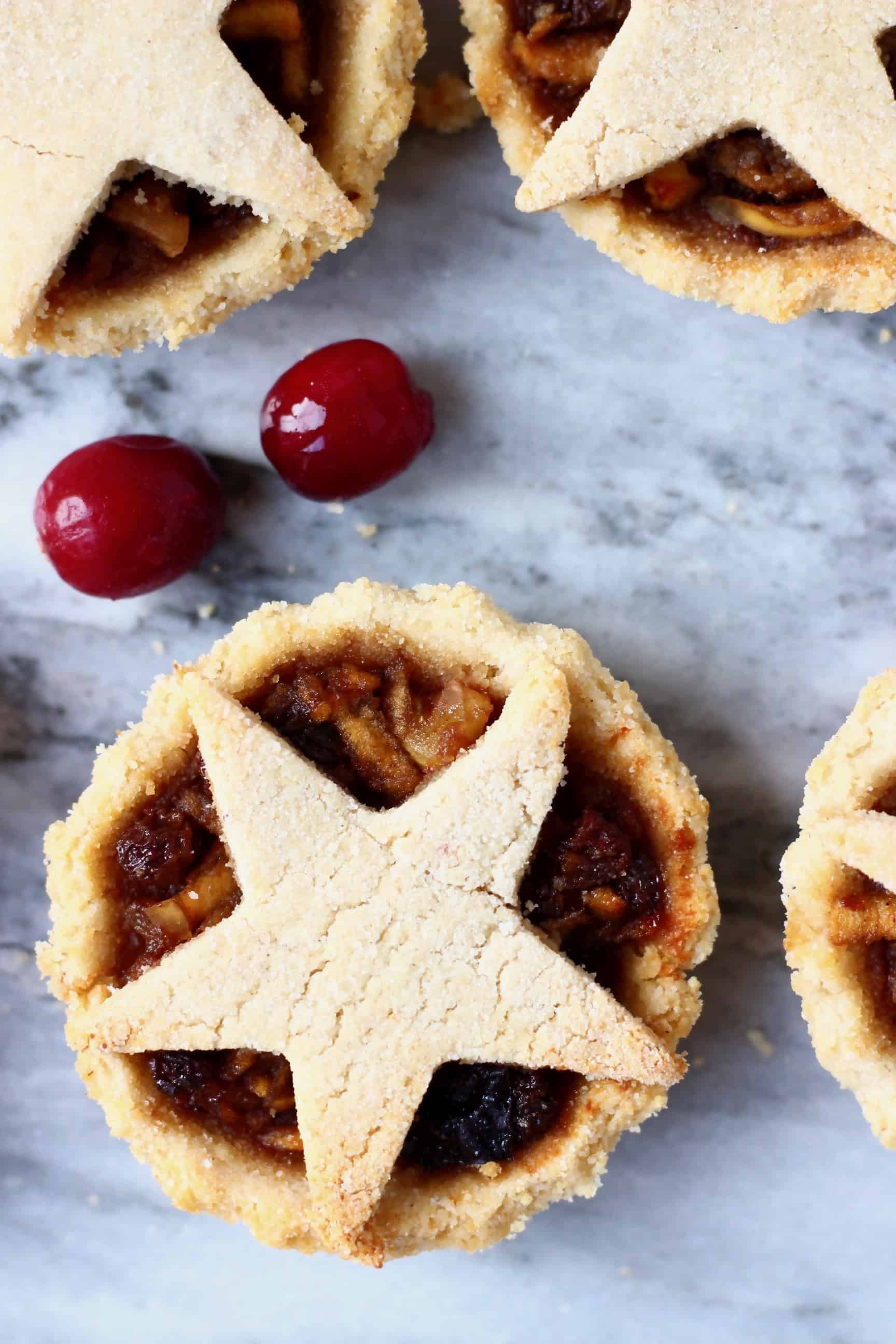 Three mince pies topped with pastry stars against a marble background scattered with fresh cranberries
