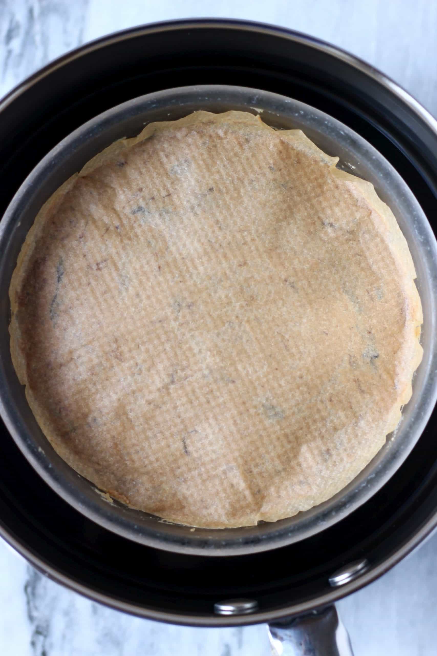 A gluten-free vegan Christmas pudding in a glass bowl in a pan covered with a circle of baking paper