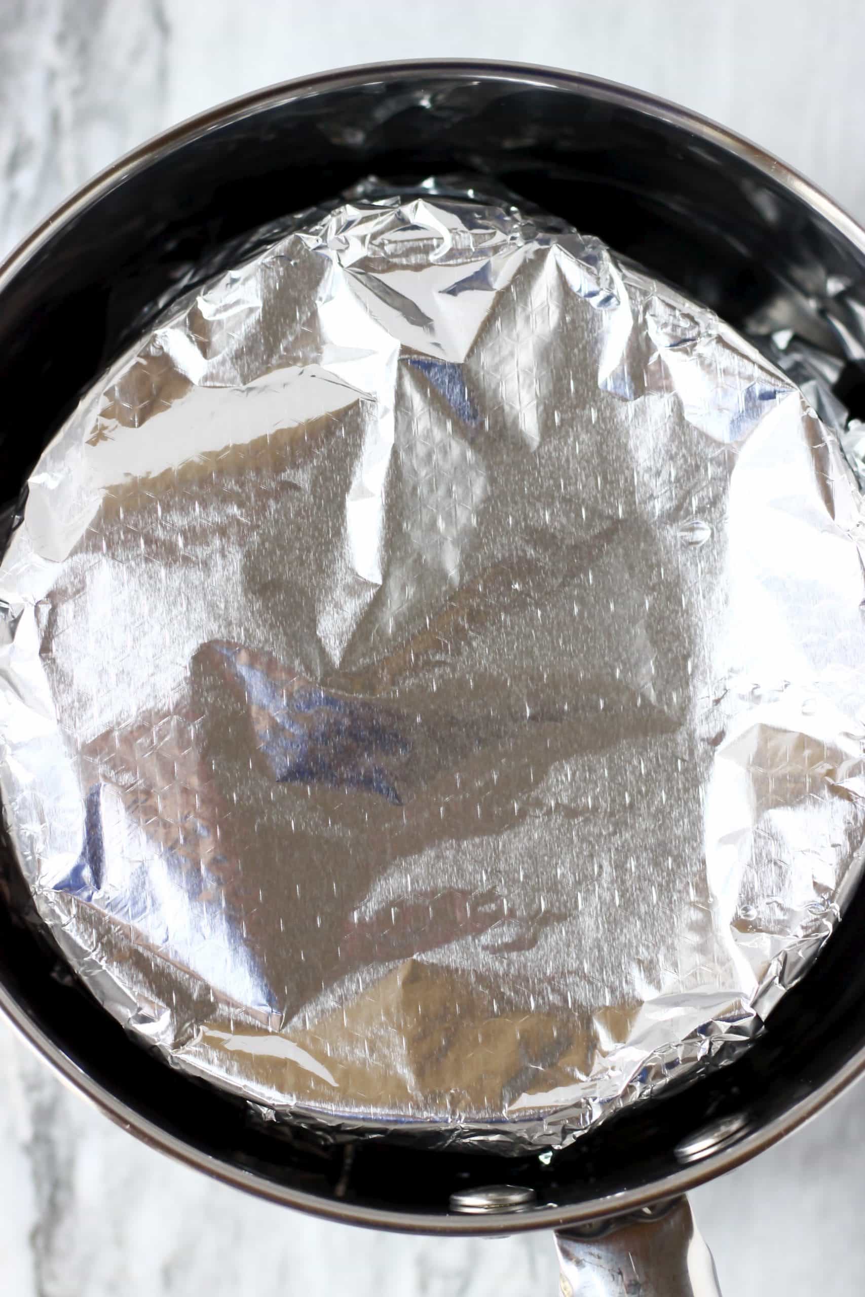 A gluten-free vegan Christmas pudding in a bowl covered with foil in a pan