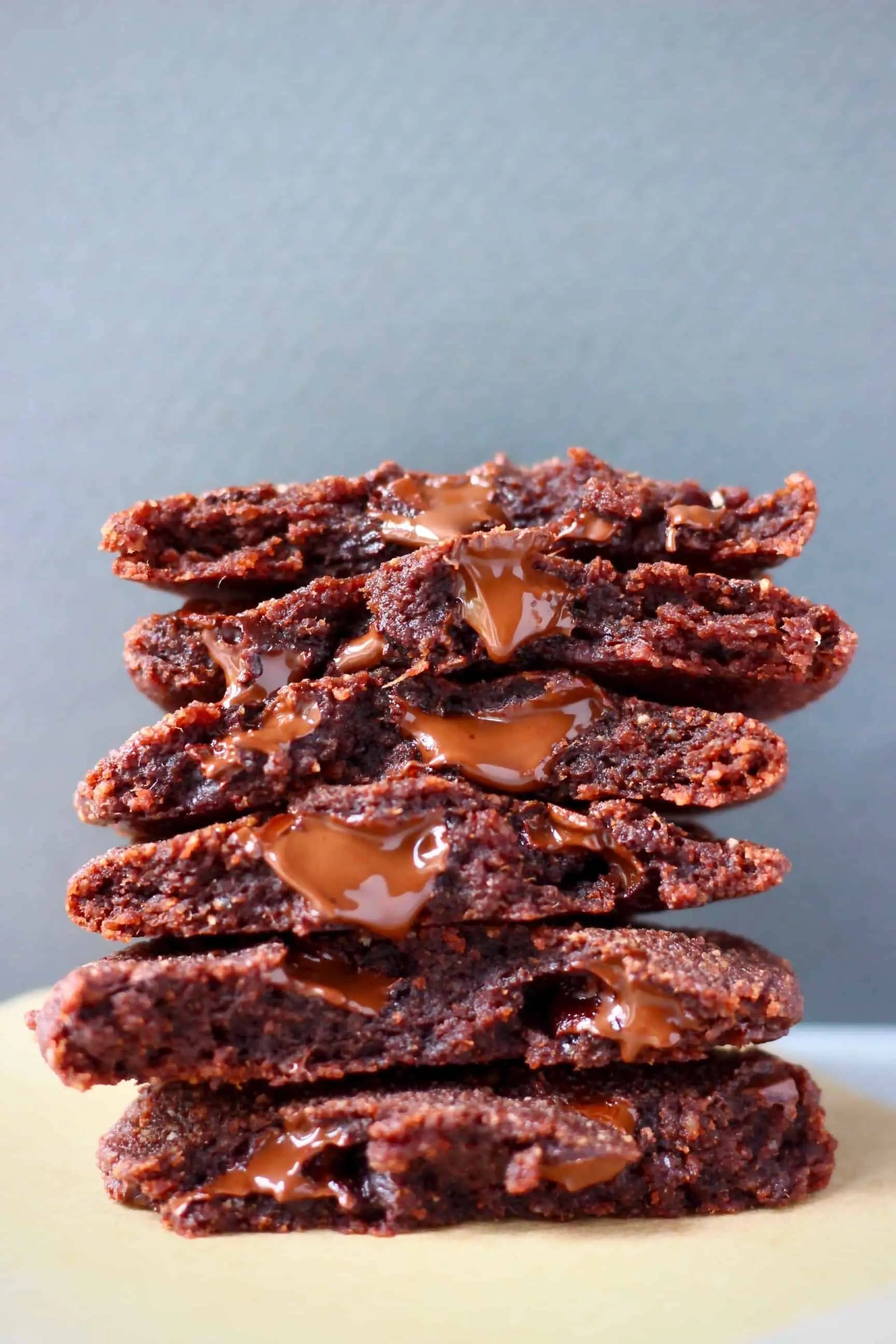A stack of six chocolate cookies on a sheet of brown baking paper against a grey background