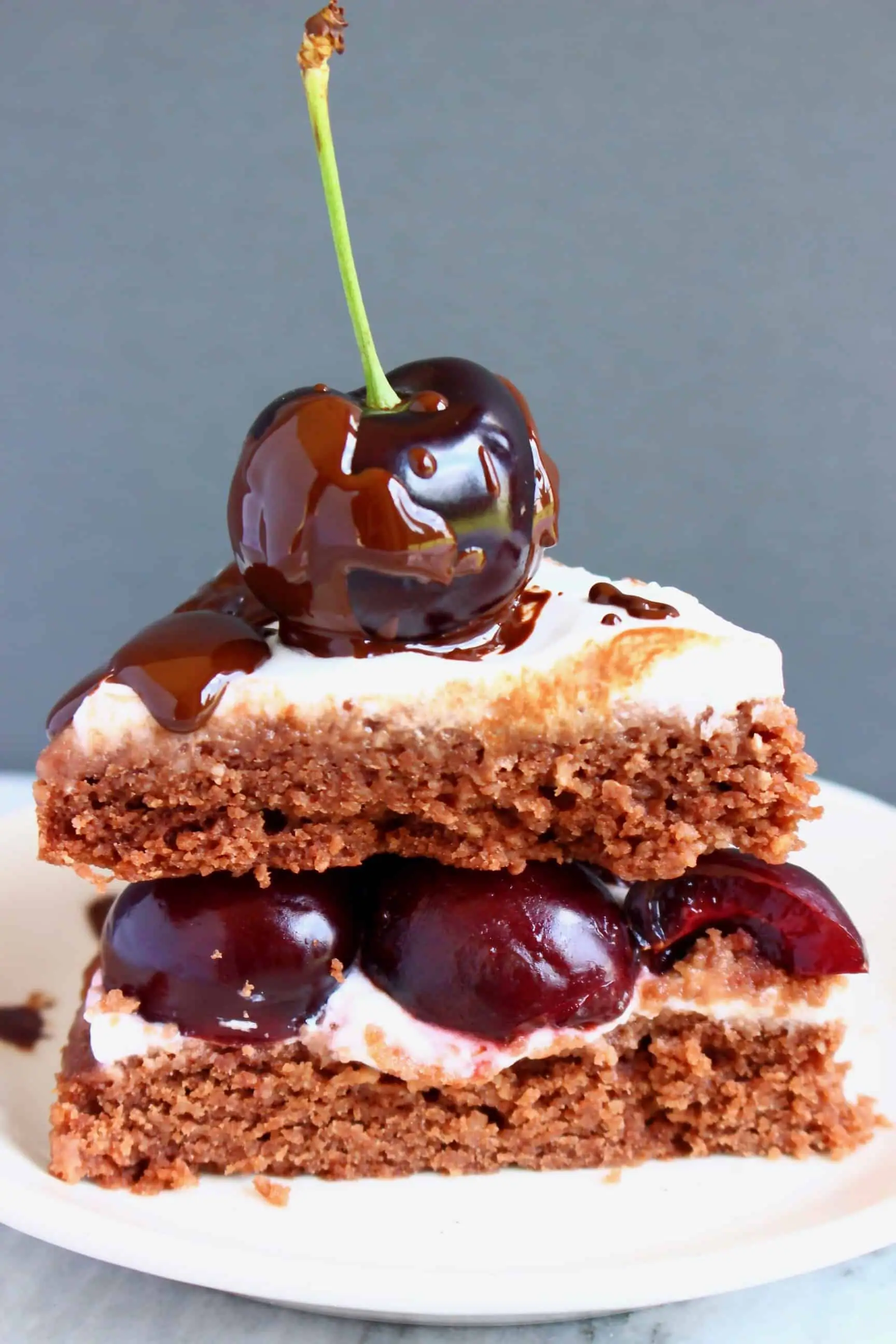 A slice of Black Forest cake sandwiched with white creamy frosting and red cherries with a whole cherry on top 