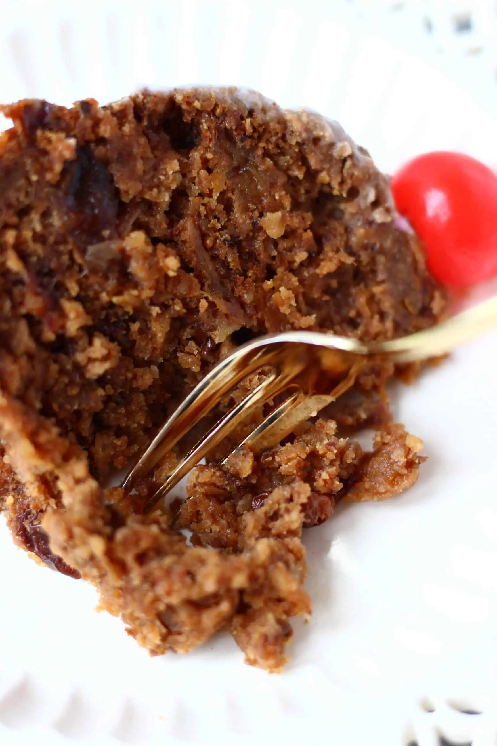 A slice of gluten-free vegan Christmas pudding on a plate with a mouthful being taken with a fork