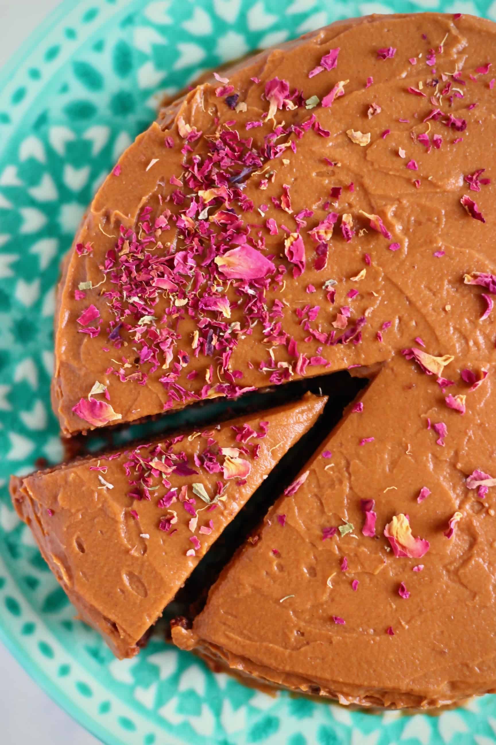 A chocolate cake with a slice taken out of it sprinkled with rose petals on a green cake stand