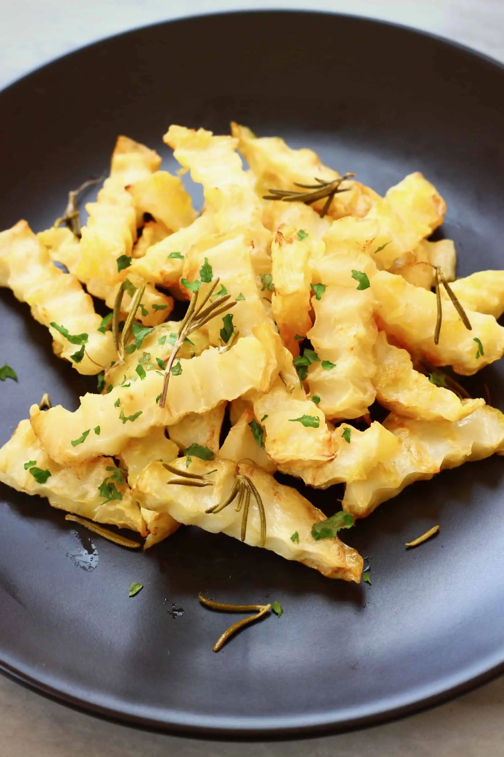 A pile of crinkle-cut celeriac fries decorated with green herbs on a black plate