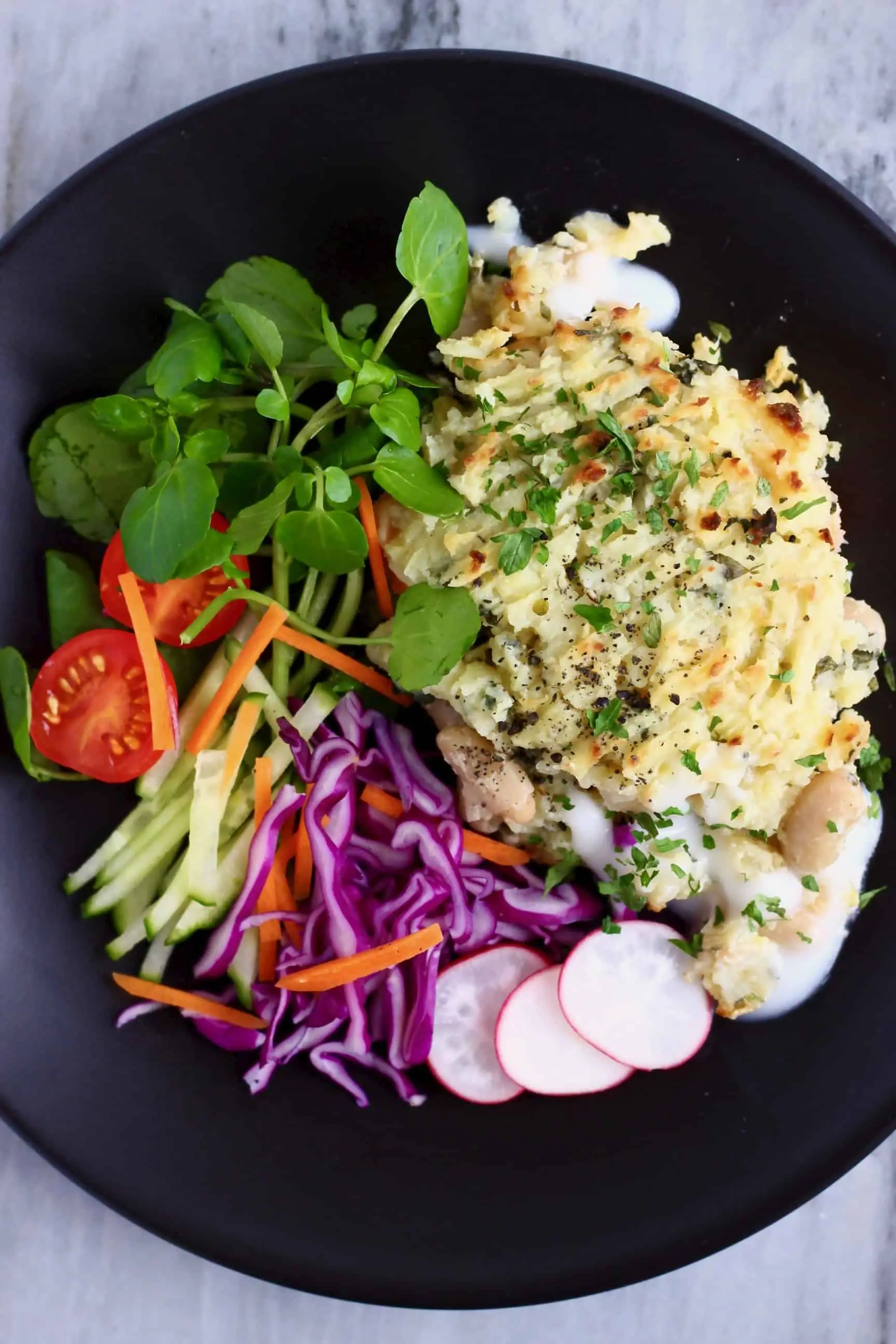 Vegan fish pie with watercress, sliced radishes and shredded purple cabbage on a black plate