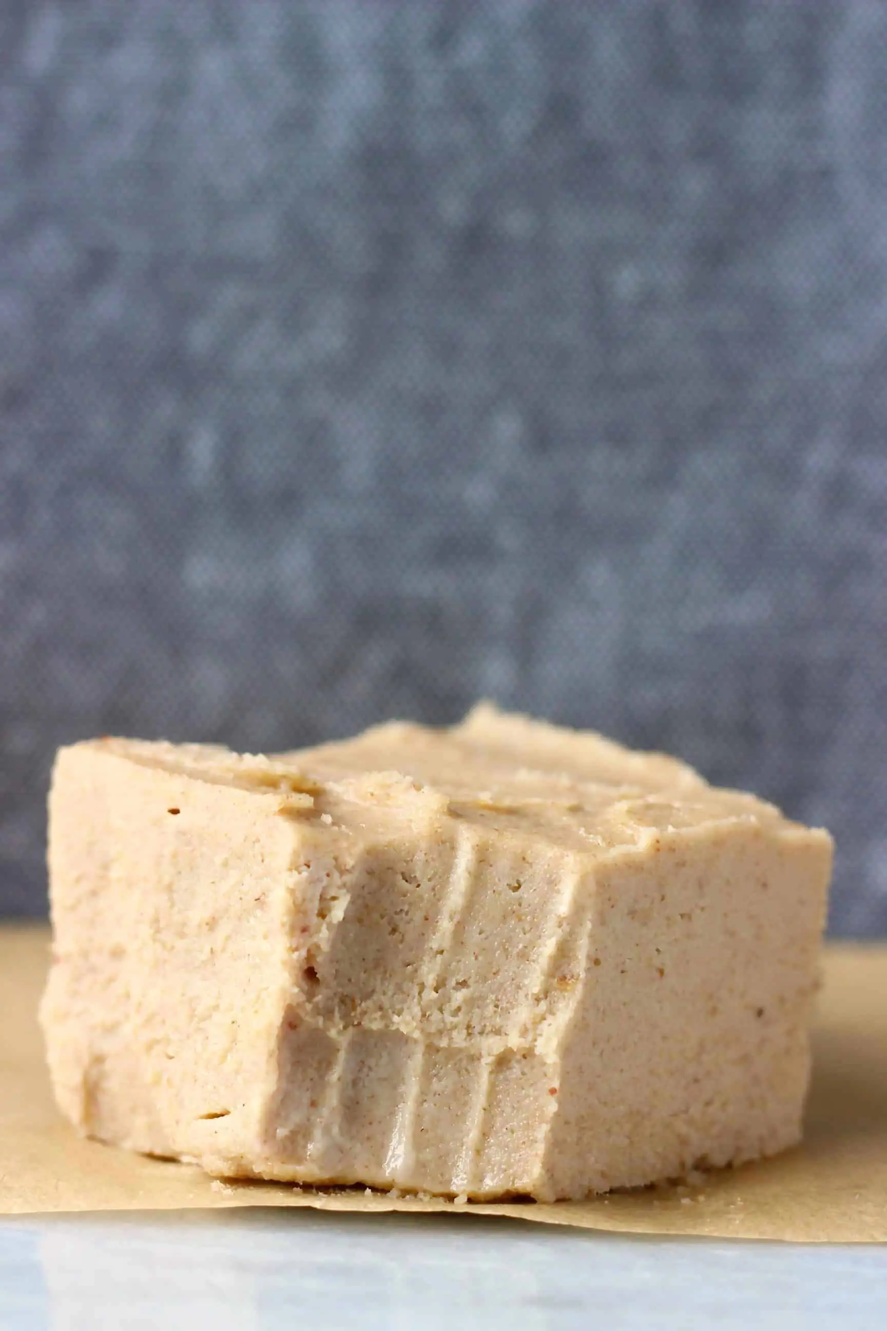 A square of caramel-coloured fudge with a bite taken out of it on a marble slab against a dark grey background