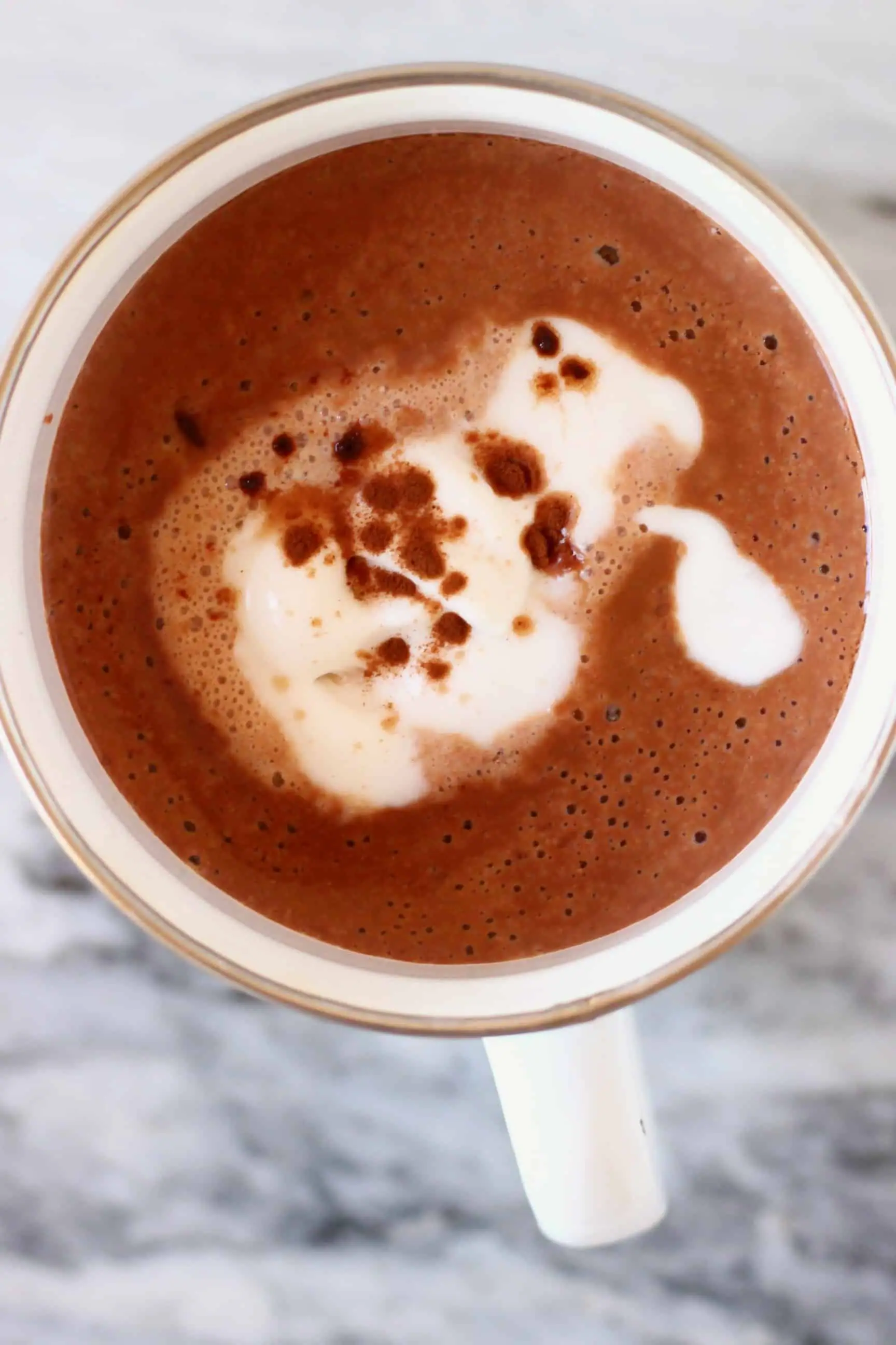 Red wine hot chocolate topped with cream and cocoa powder in a white mug against a marble background