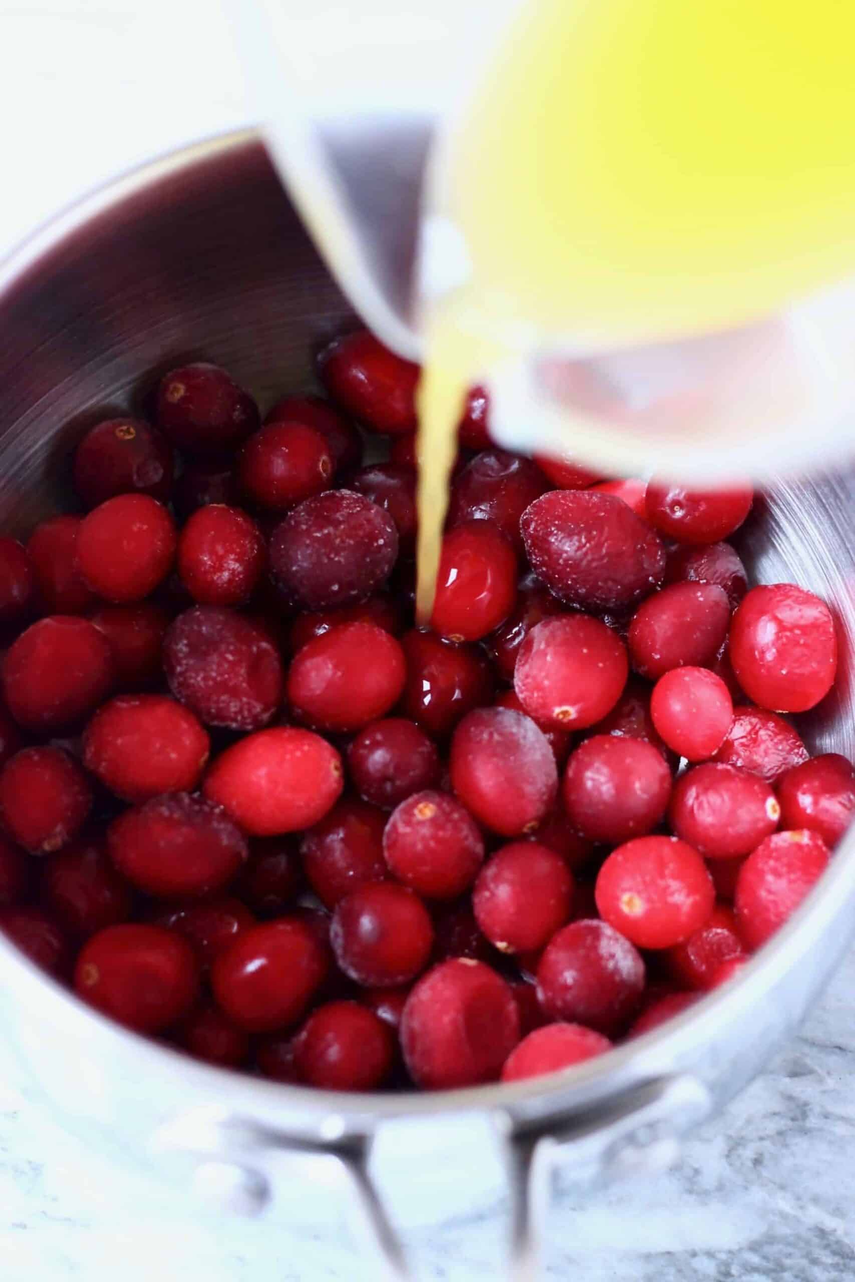 Fresh cranberries in a pan with orange juice being poured in from a jug