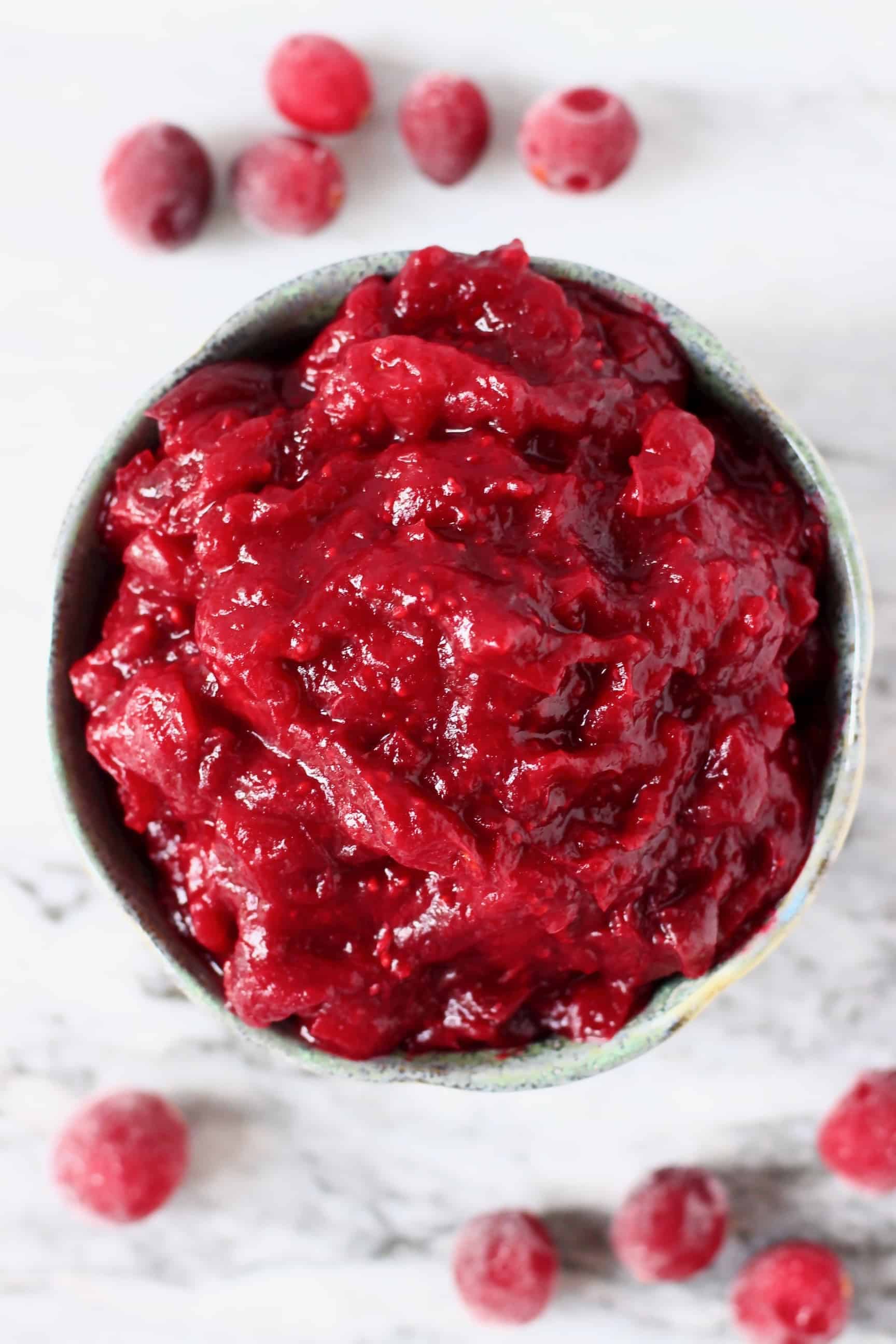 Cranberry sauce in a blue bowl against a marble background with fresh cranberries around