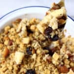 Gluten-free vegan stuffing with chestnuts, apple and dried cherries in a pie dish with a spoon holding up a mouthful