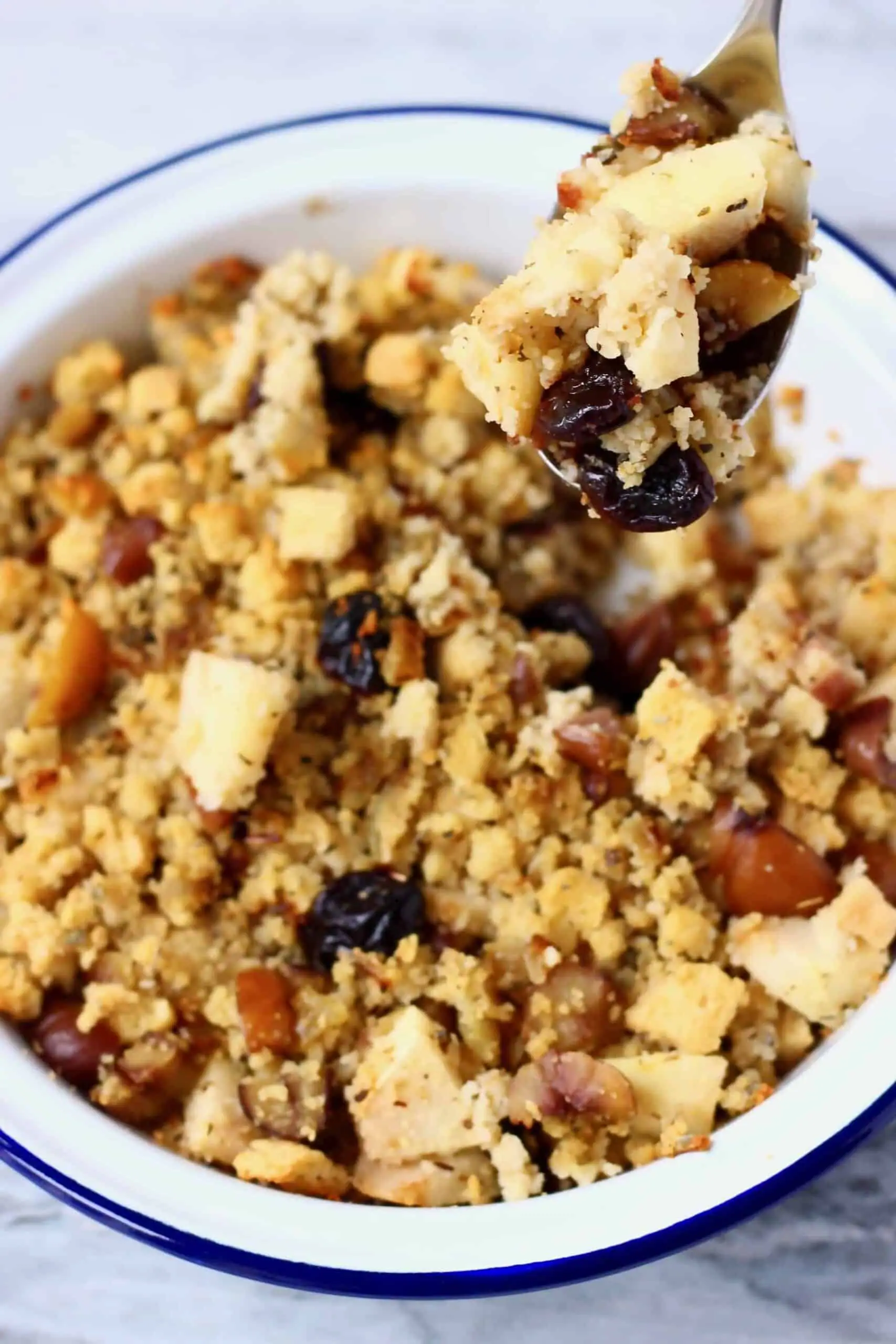 Gluten-free vegan stuffing with chestnuts, apple and dried cherries in a pie dish with a spoon holding up a mouthful