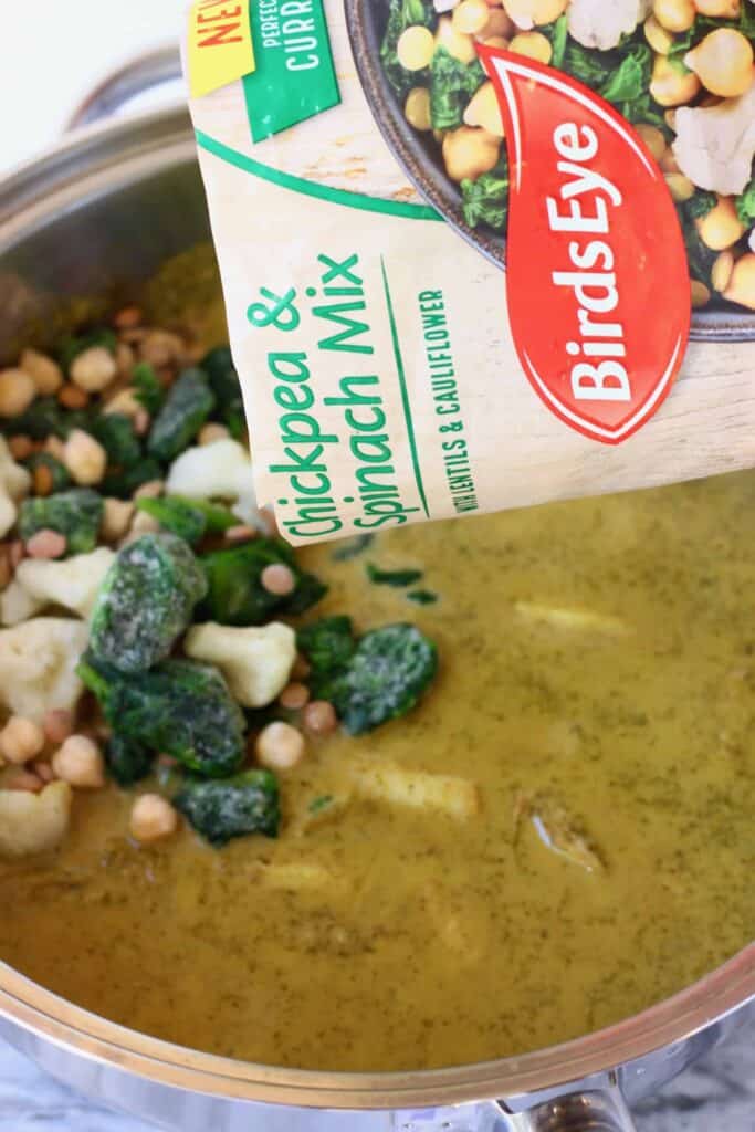 Photo of Birds Eye Chickpea & Spinach Mix being poured into a green curry sauce in a silver saucepan