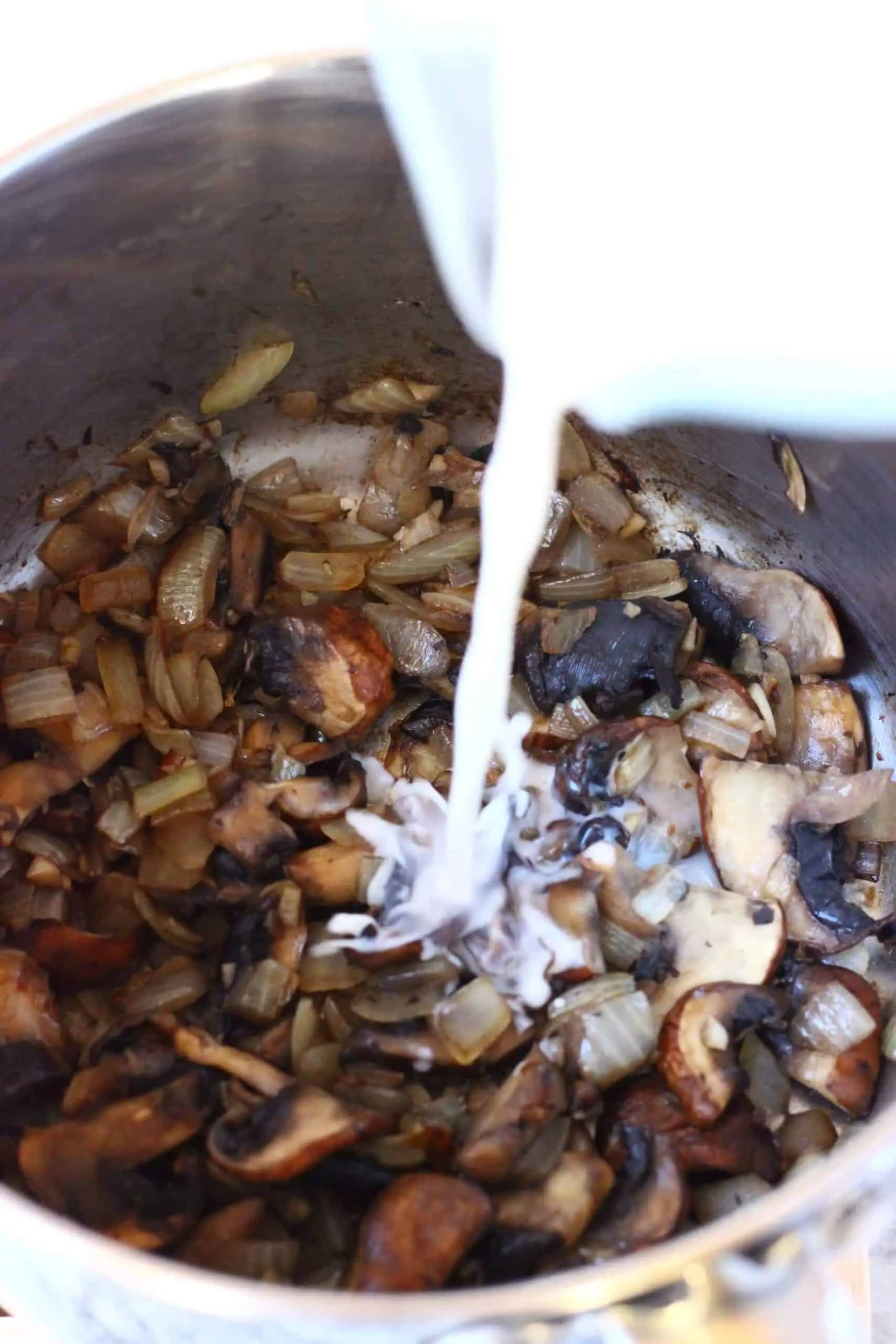 Sliced mushrooms in a pan with almond milk being poured into it